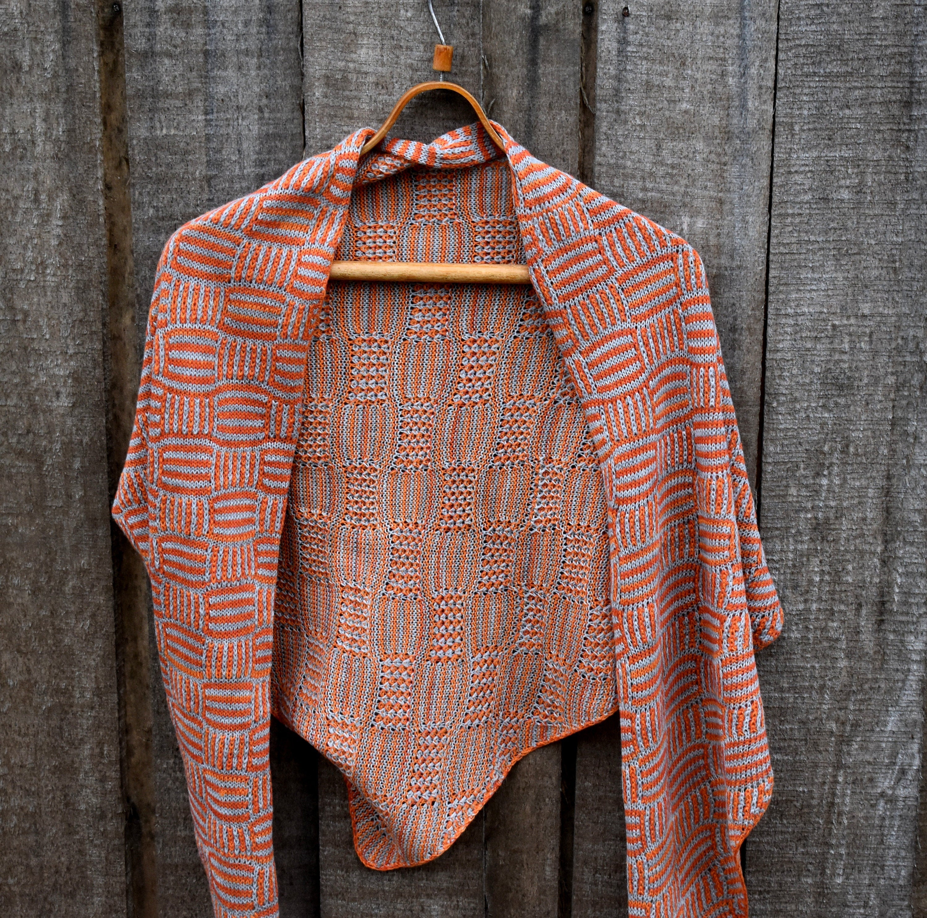 Knitted shawl with orange and brown pattern on a wooden hanger against a wooden background