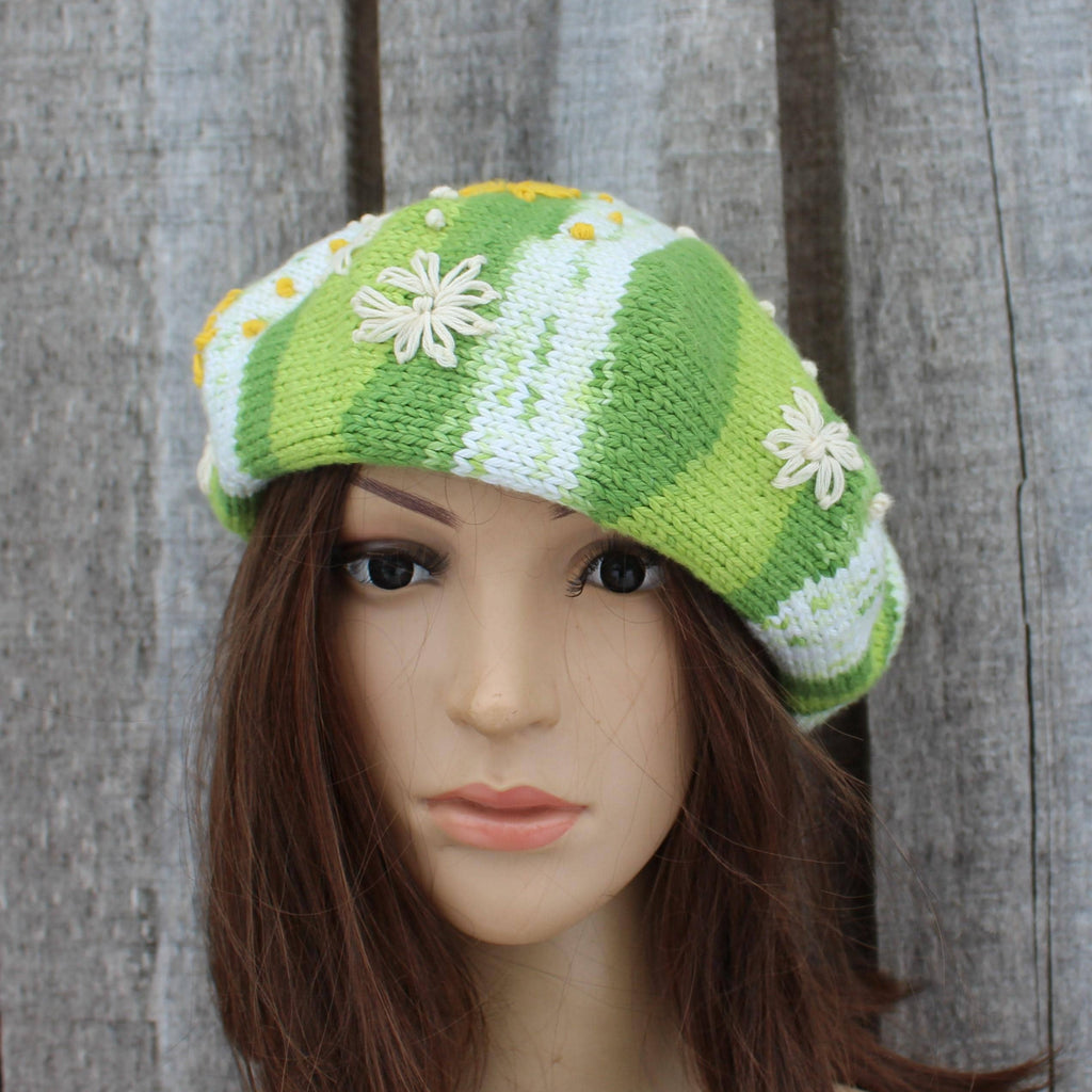 Green and white knitted hat with floral patterns on a mannequin head against a wooden background