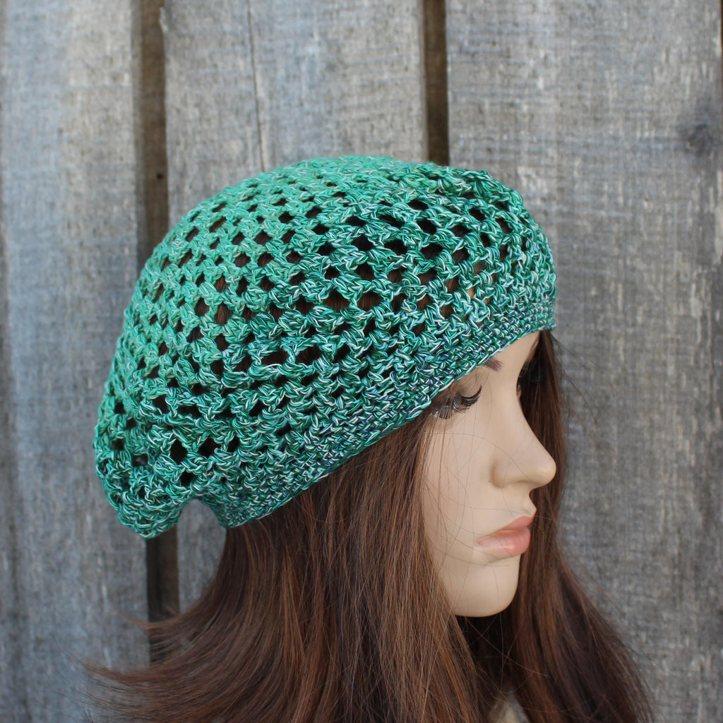 Green crocheted beret worn by a mannequin against a wooden background