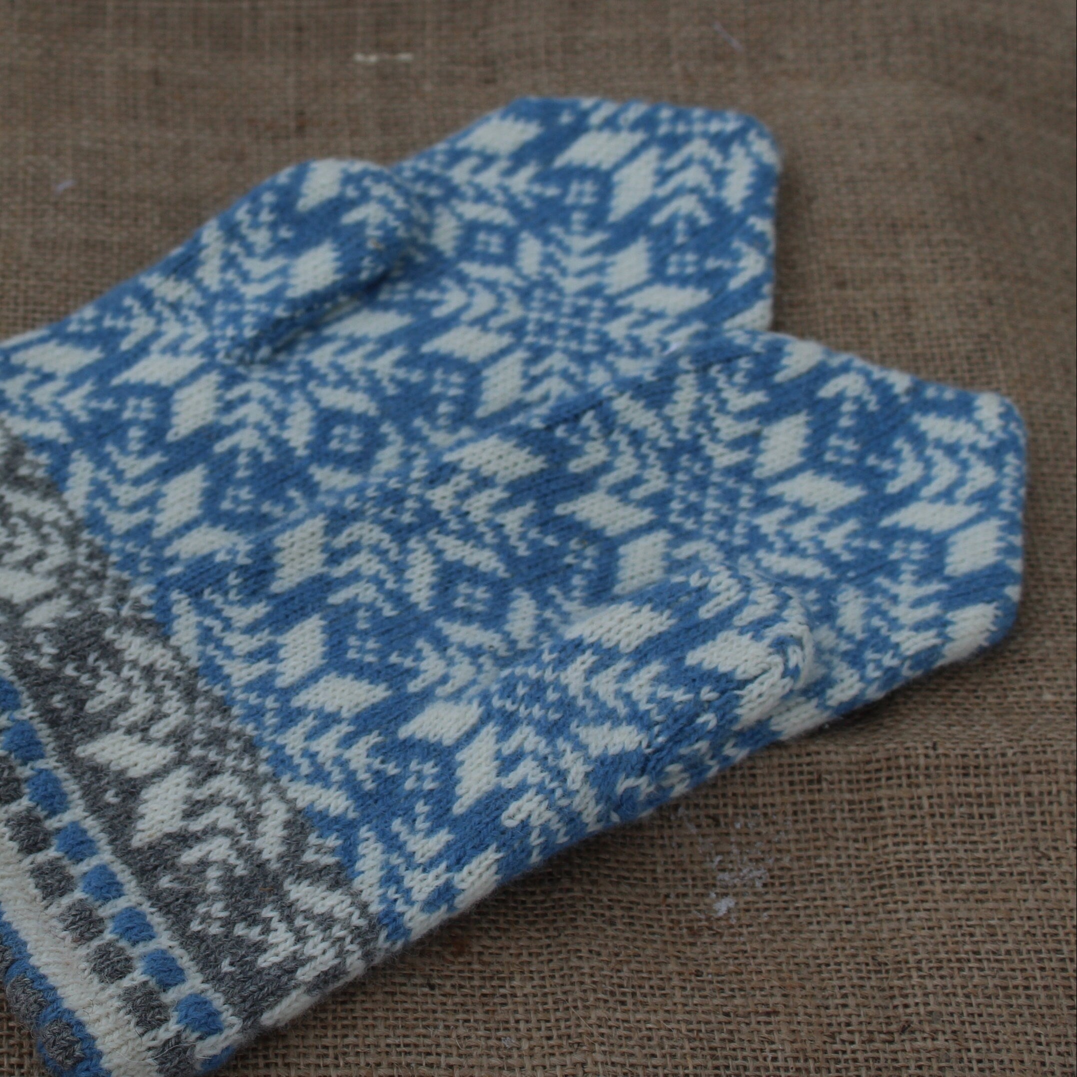 Pair of blue and gray patterned mittens on a brown fabric background