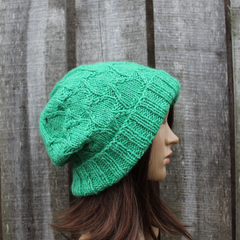 Green knitted beanie worn by a mannequin against a wooden background