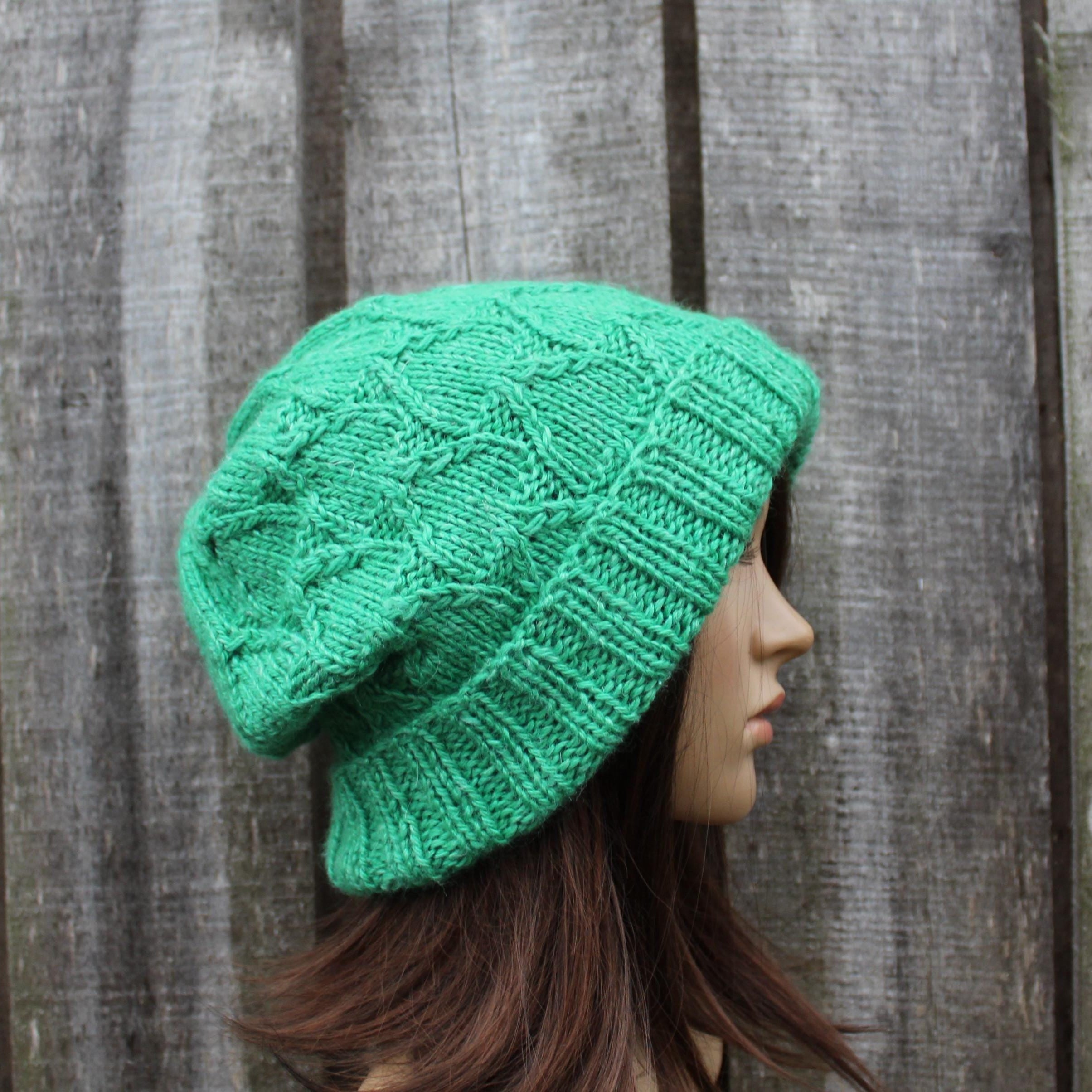 Green knitted beanie worn by a mannequin against a wooden background