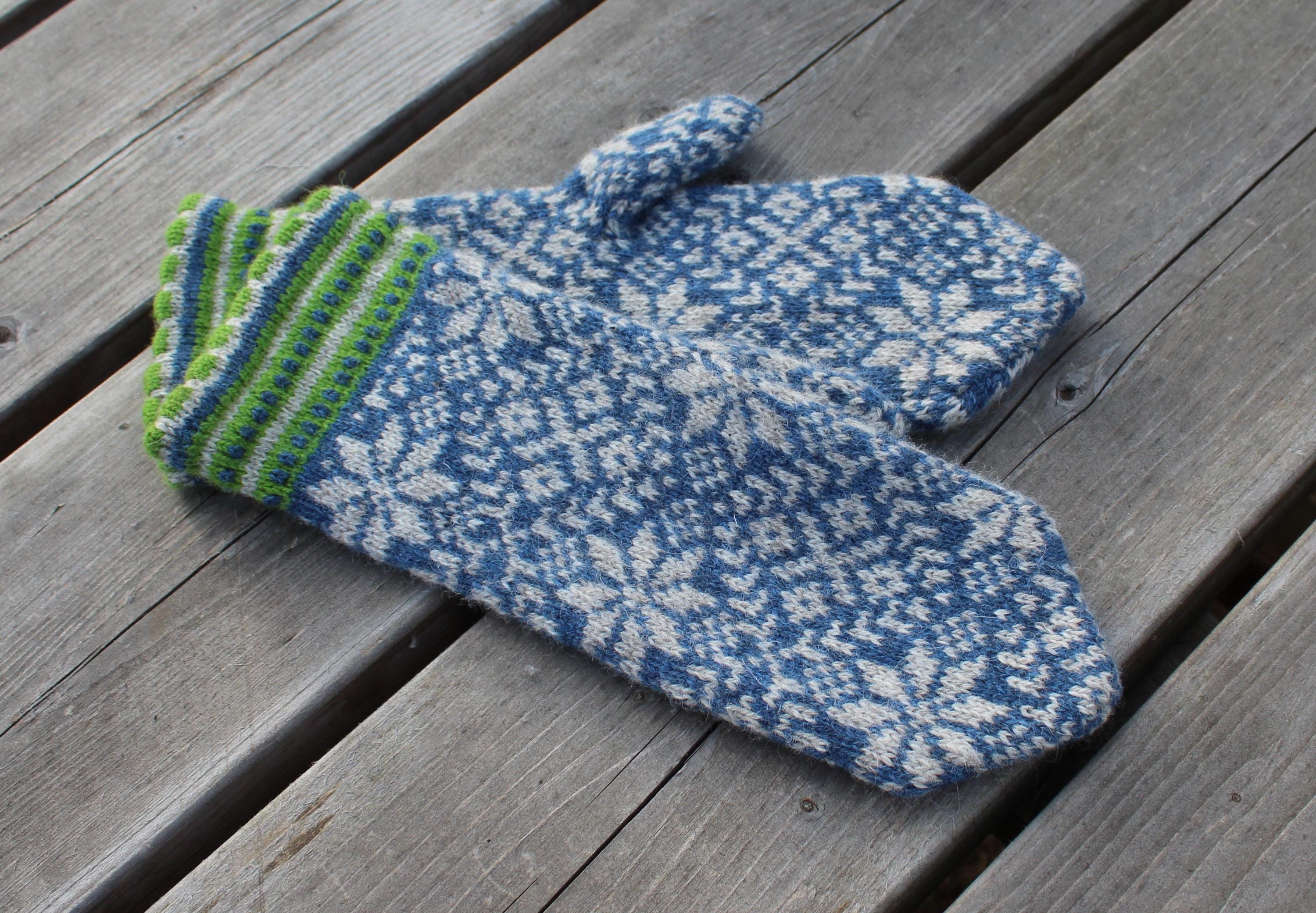 Pair of blue and white patterned mittens with green stripes on a wooden surface
