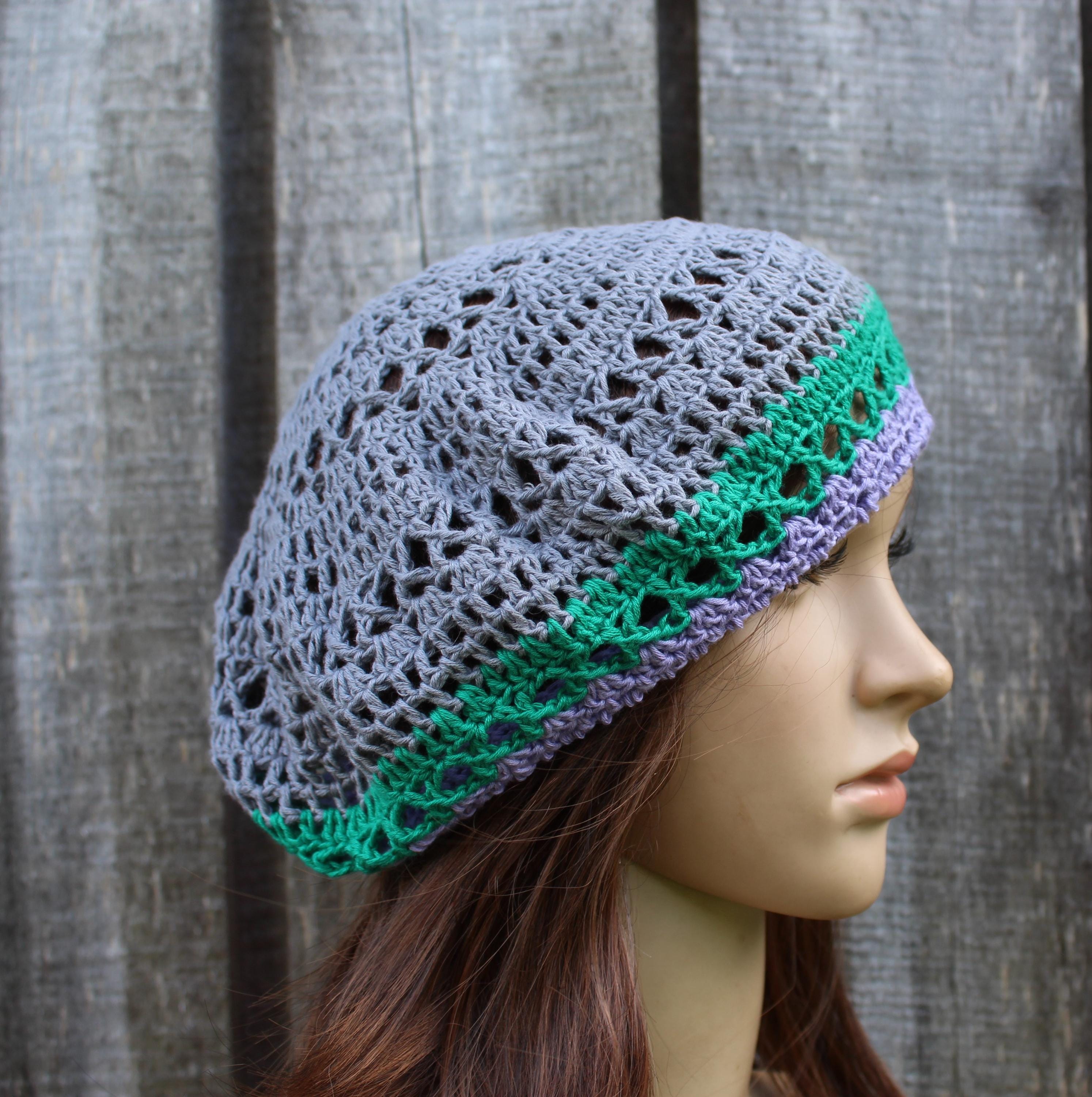 Crocheted hat with gray, green, and purple pattern on a mannequin head against a wooden background