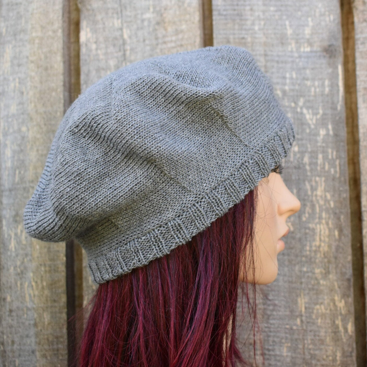Person wearing a gray knit beanie against a wooden background
