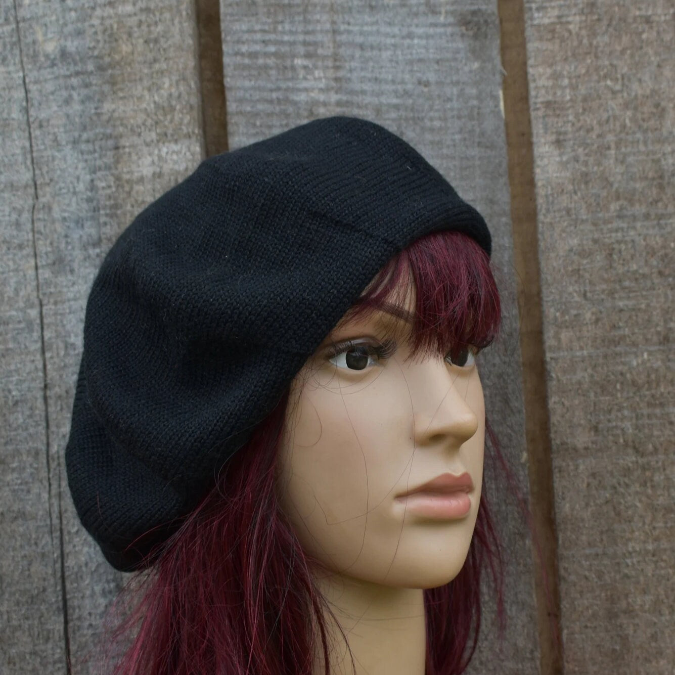 Black beret on a mannequin head with red hair against a wooden background