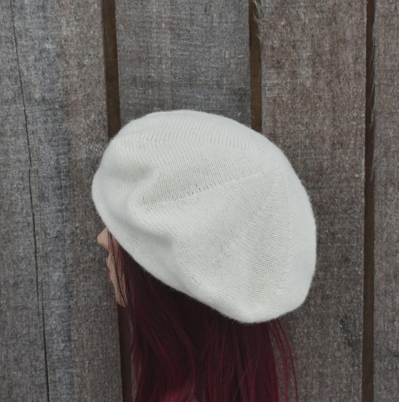 Person wearing a white knit beanie against a wooden background