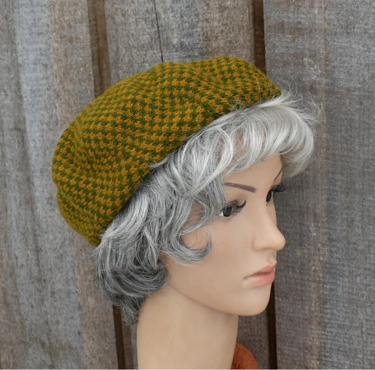 Green knitted beret on a mannequin head with gray hair against a wooden background