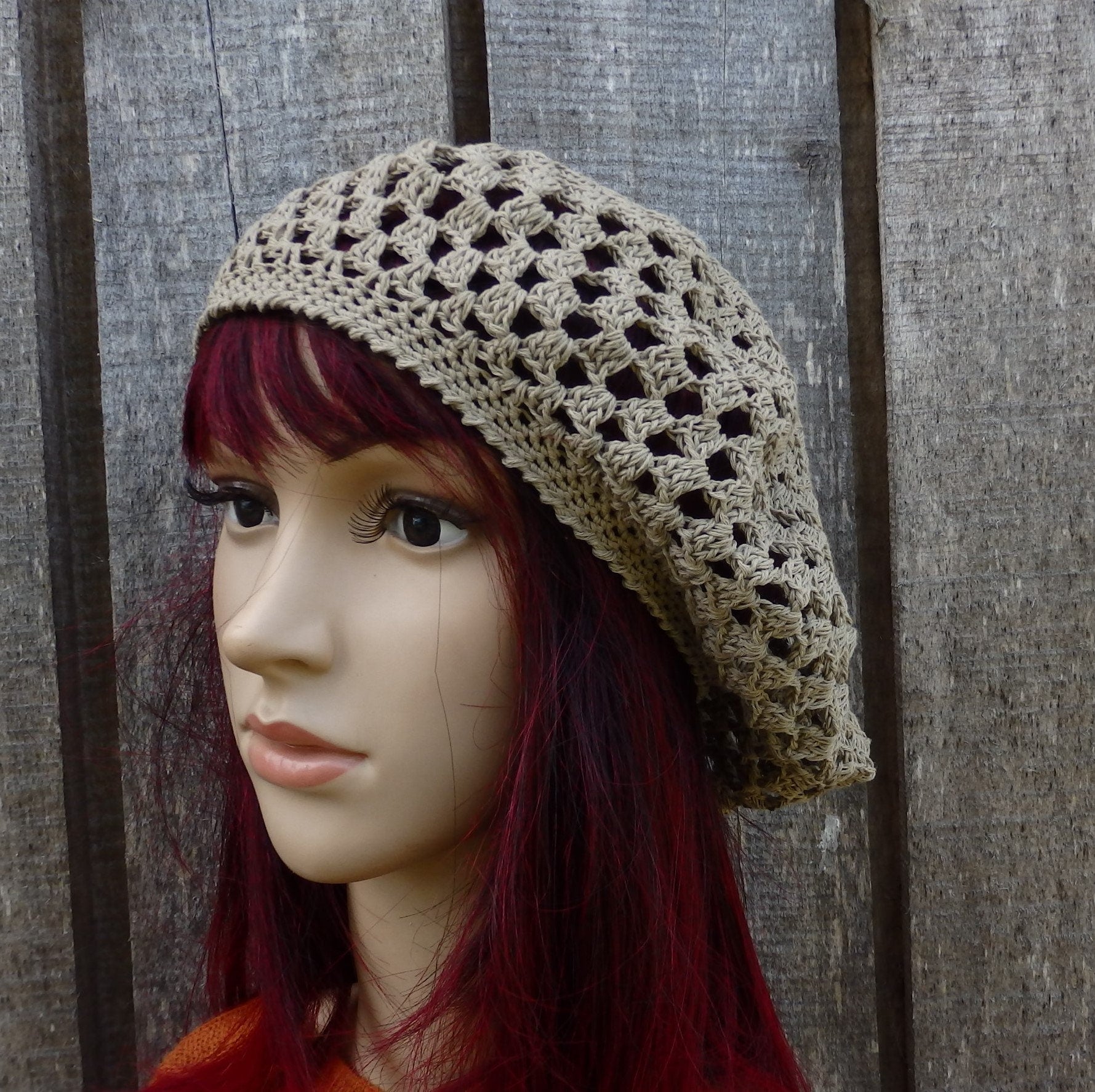 Mannequin head wearing a beige crochet hat against a wooden background