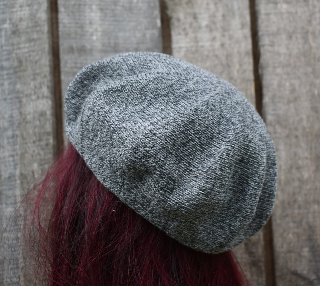 Gray knit beret worn by a person with red hair against a wooden background