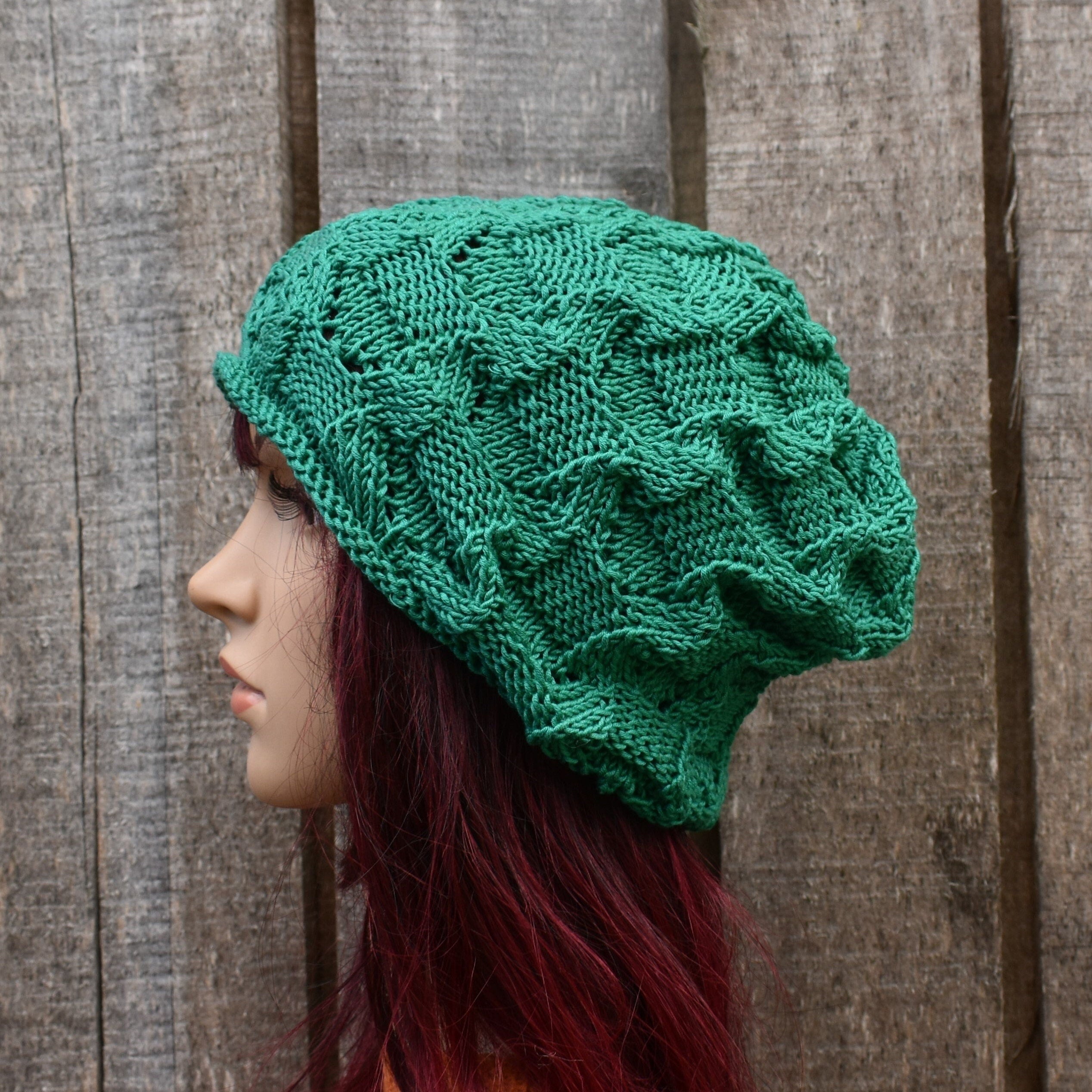 Green knitted hat worn by a person with red hair against a wooden background