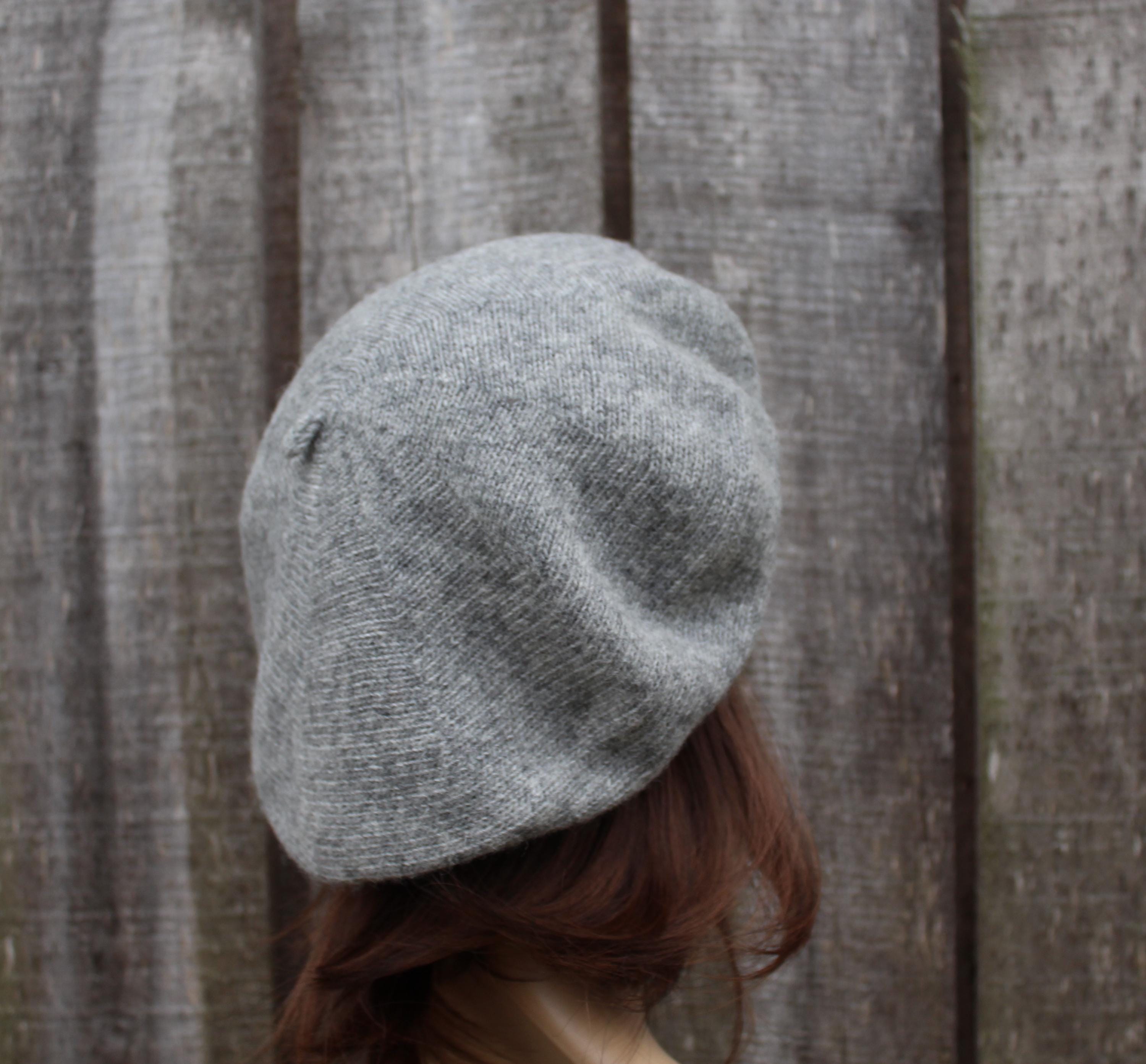 Person wearing a gray knit beret against a wooden fence background