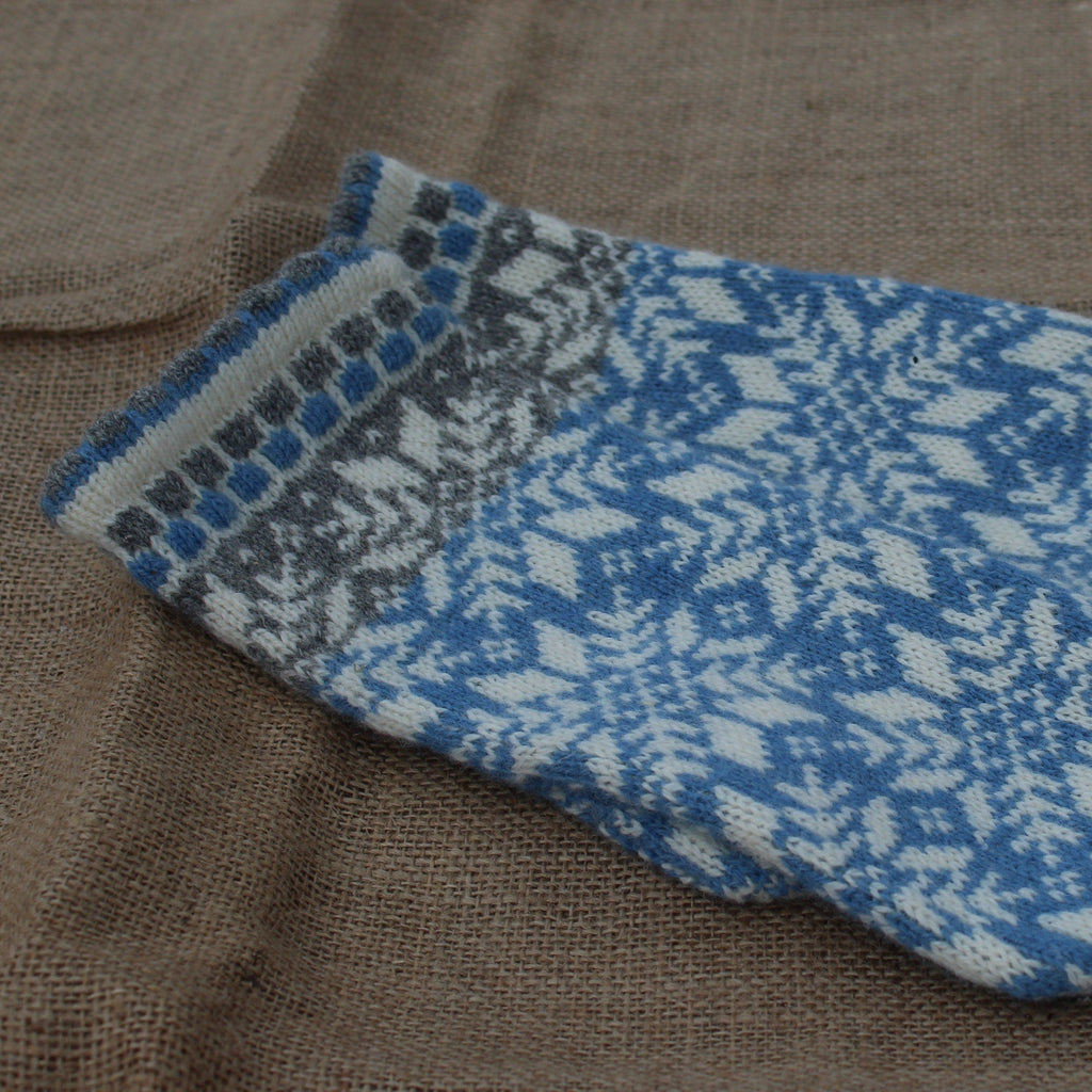 Knitted blue and gray patterned mitten on a textured brown surface