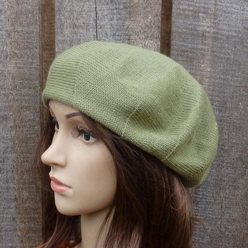 Green knitted beret on a mannequin head against a textured brown background