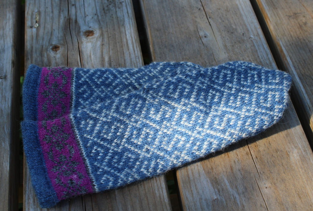 Blue knitted mitten with purple trim on a wooden surface