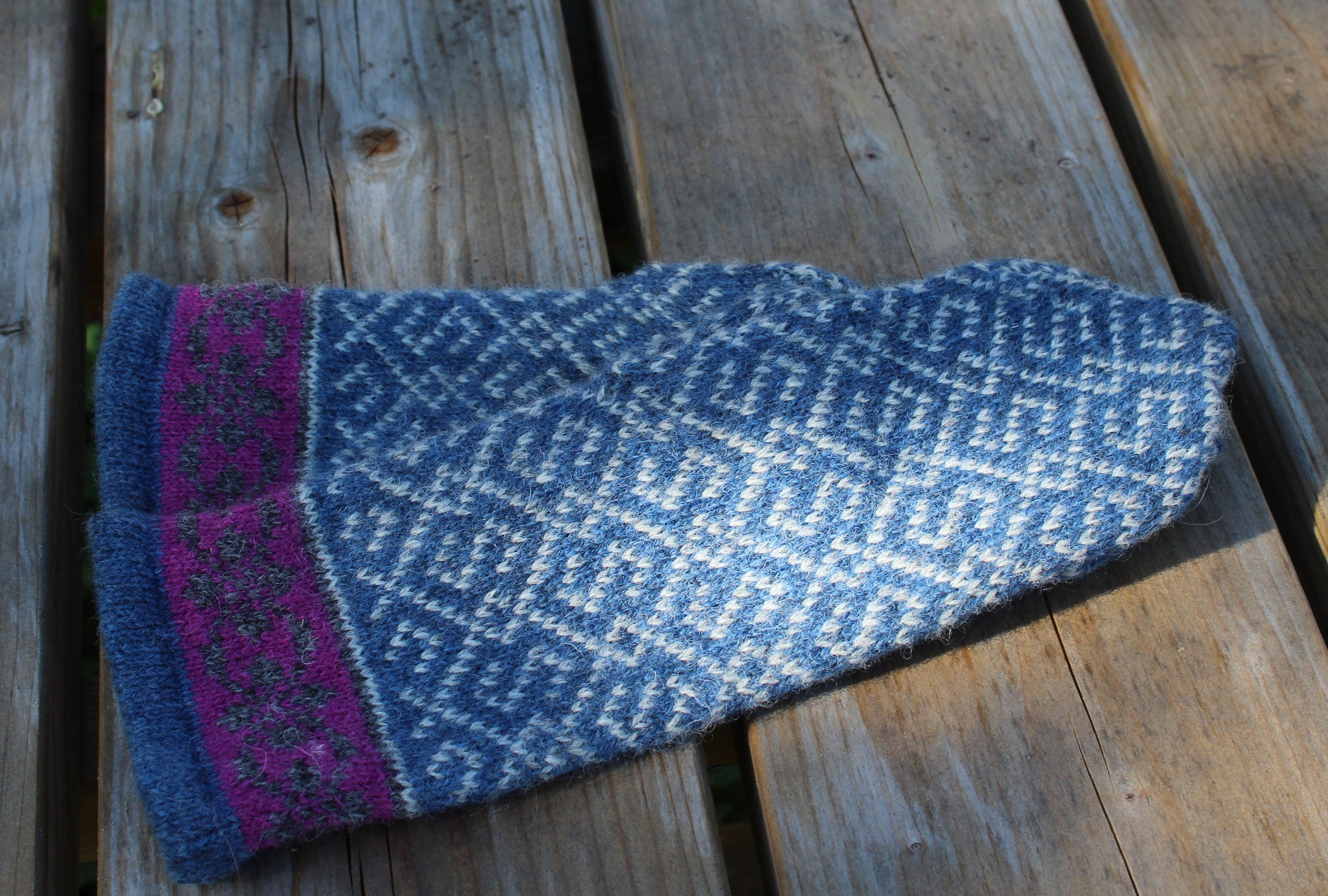 Blue knitted mitten with purple trim on a wooden surface