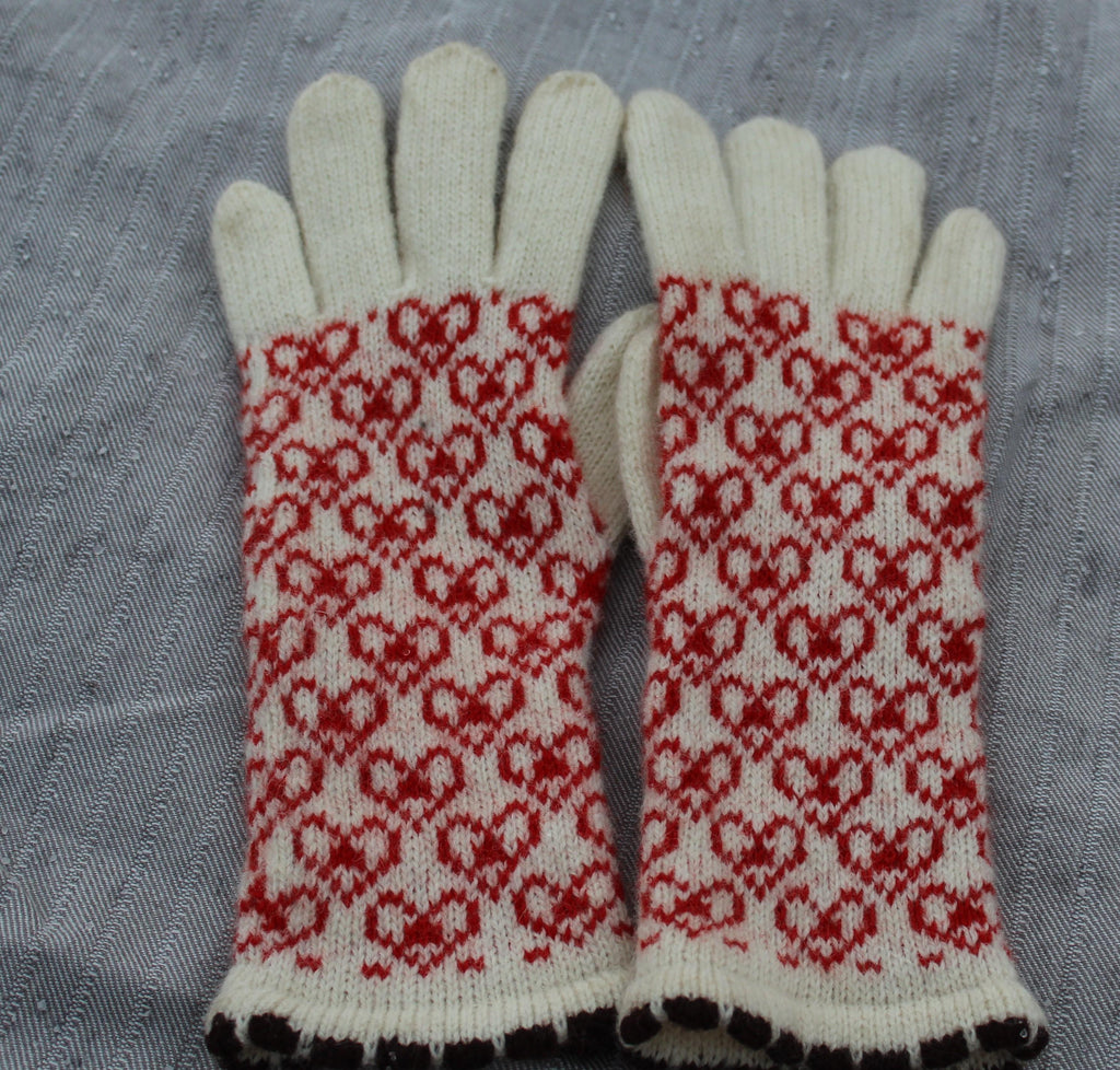 Pair of knitted gloves with red and white pattern on a gray background