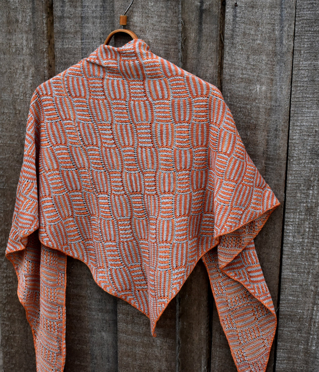 Knitted shawl with a geometric pattern hanging on a wooden hook against a wooden background