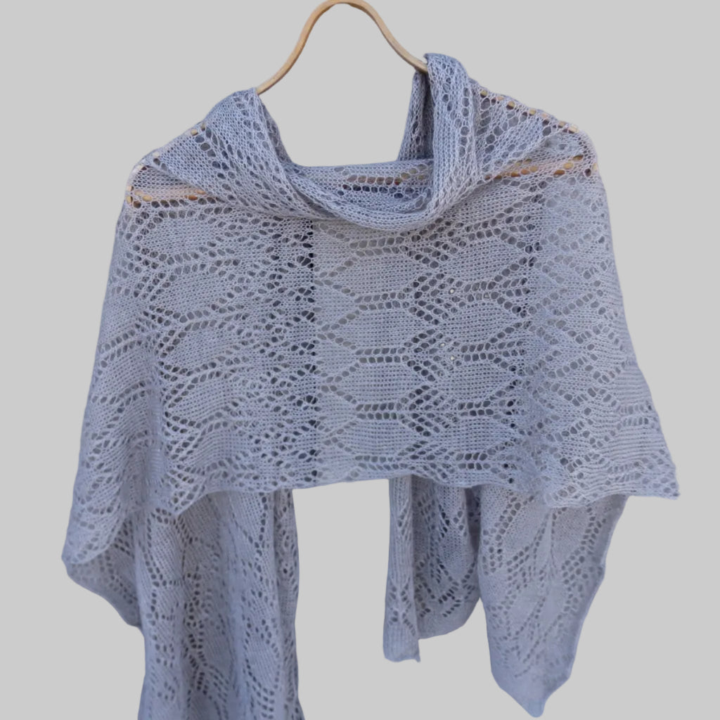 Knitted shawl on a wooden hanger against a wooden background