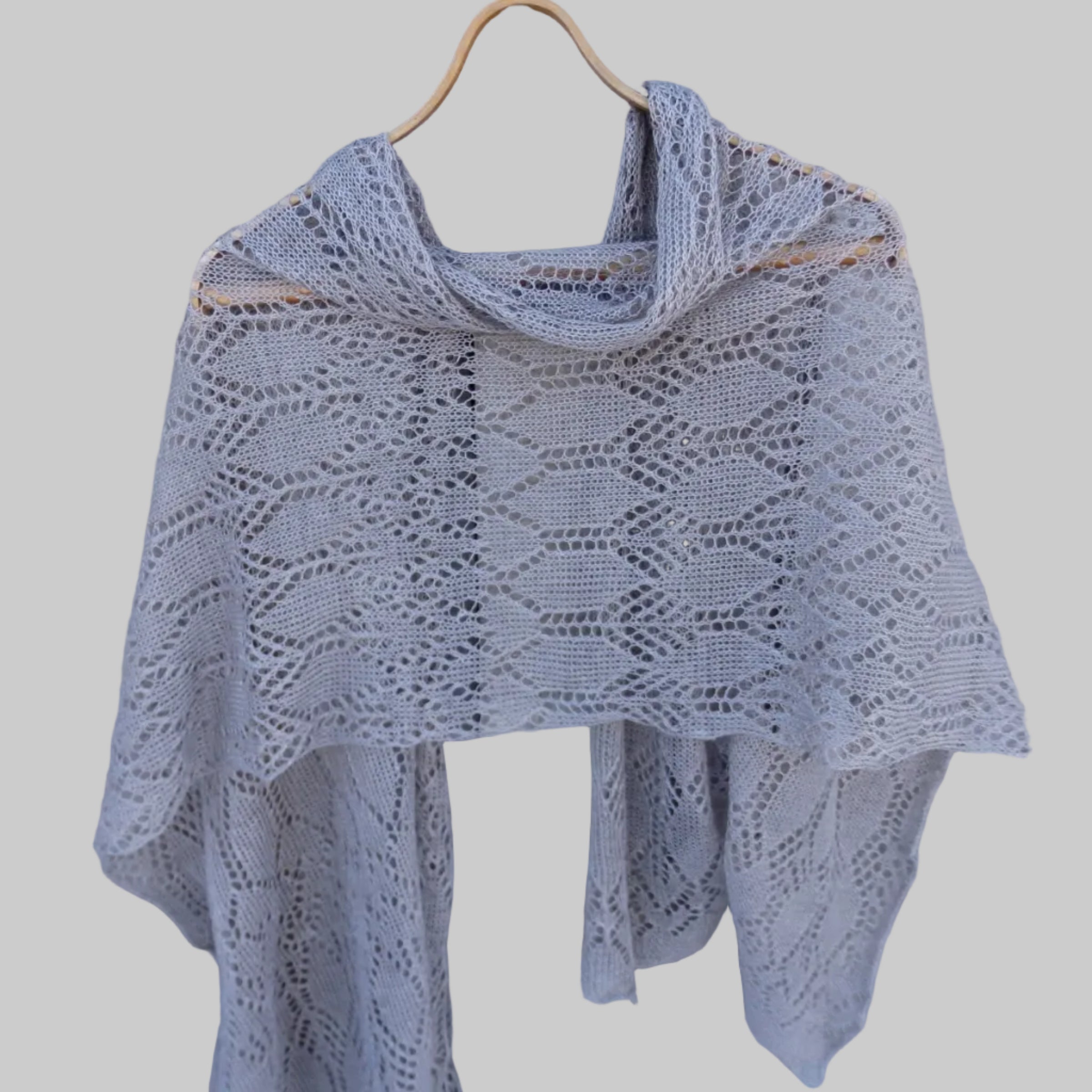 Knitted shawl on a wooden hanger against a wooden background
