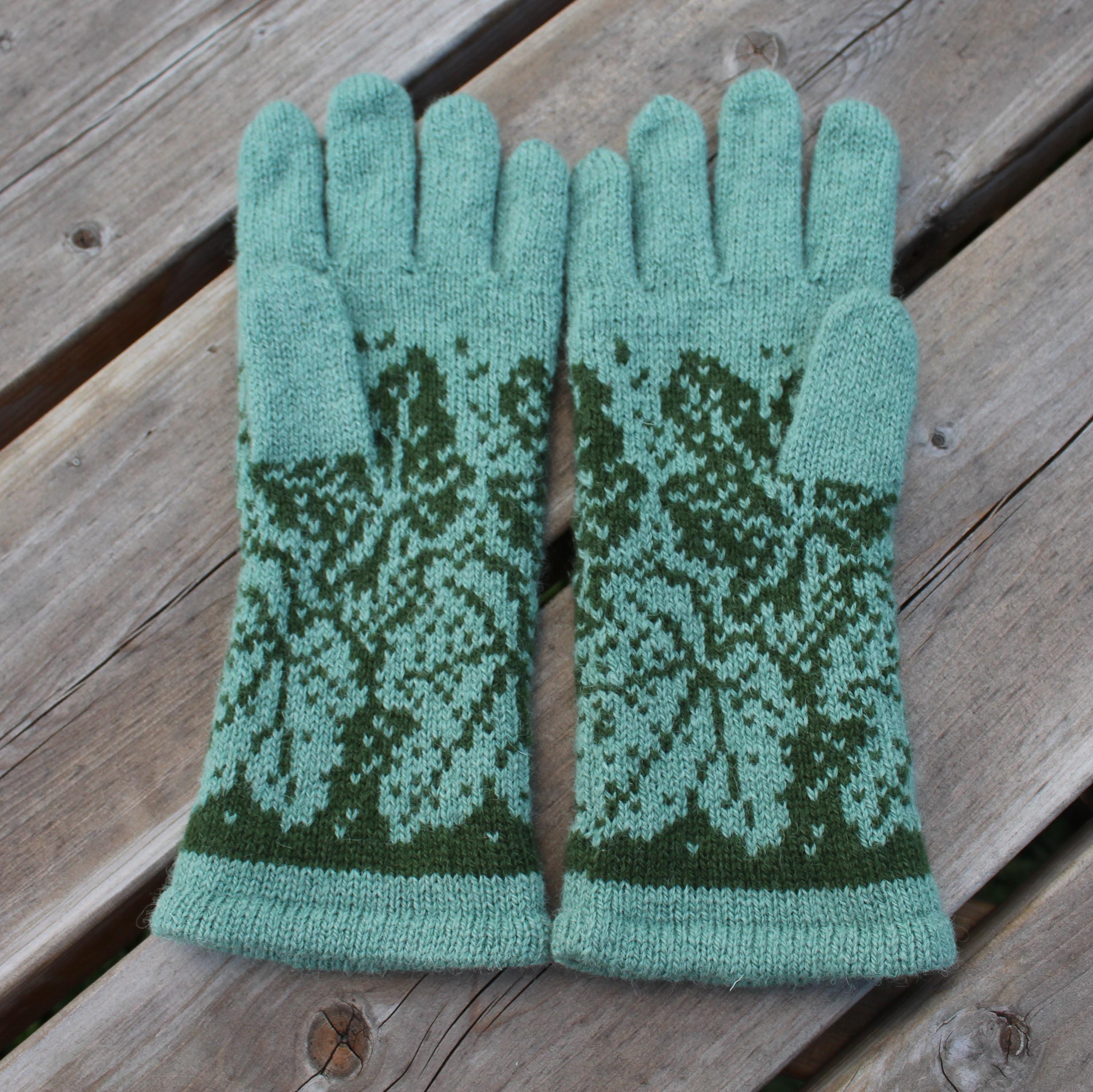 Pair of green knitted gloves with a pattern on a wooden surface