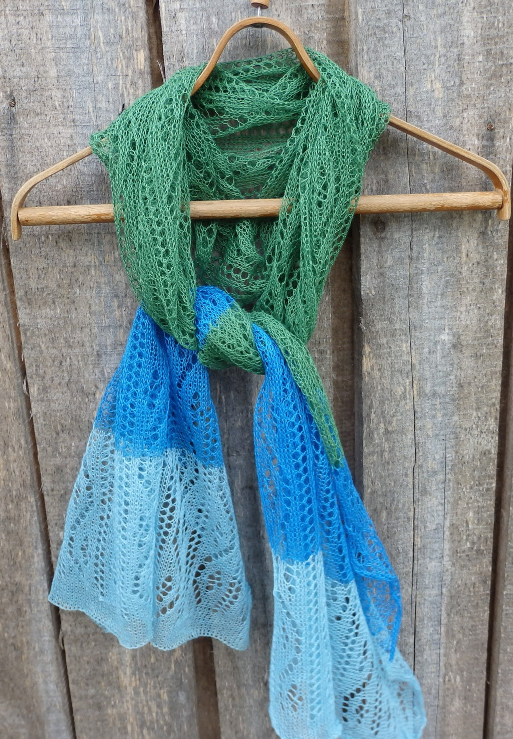 Green and blue lace scarf on a wooden hanger against a wooden background