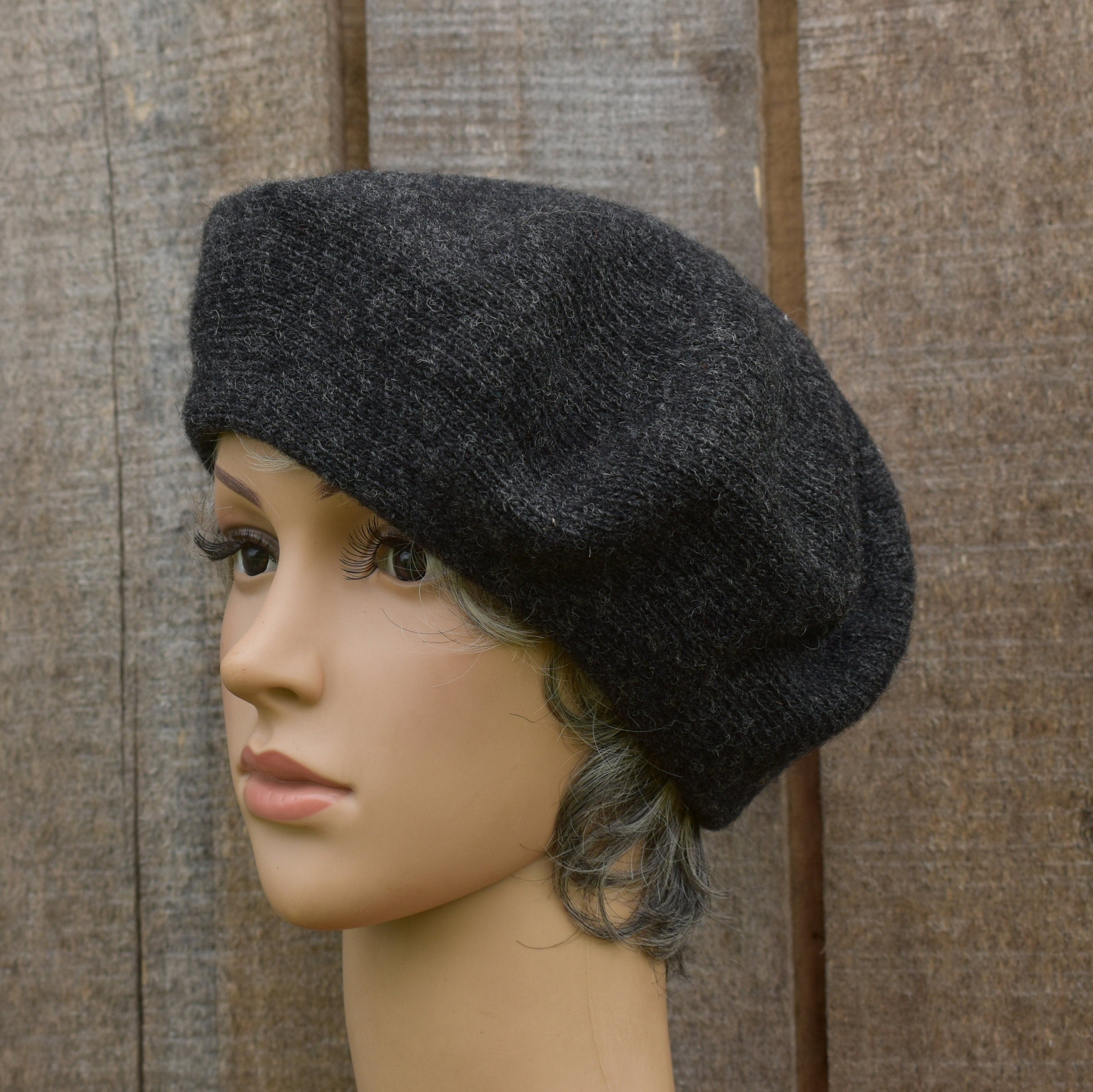 Dark gray knit beret on a mannequin head against a wooden panel background