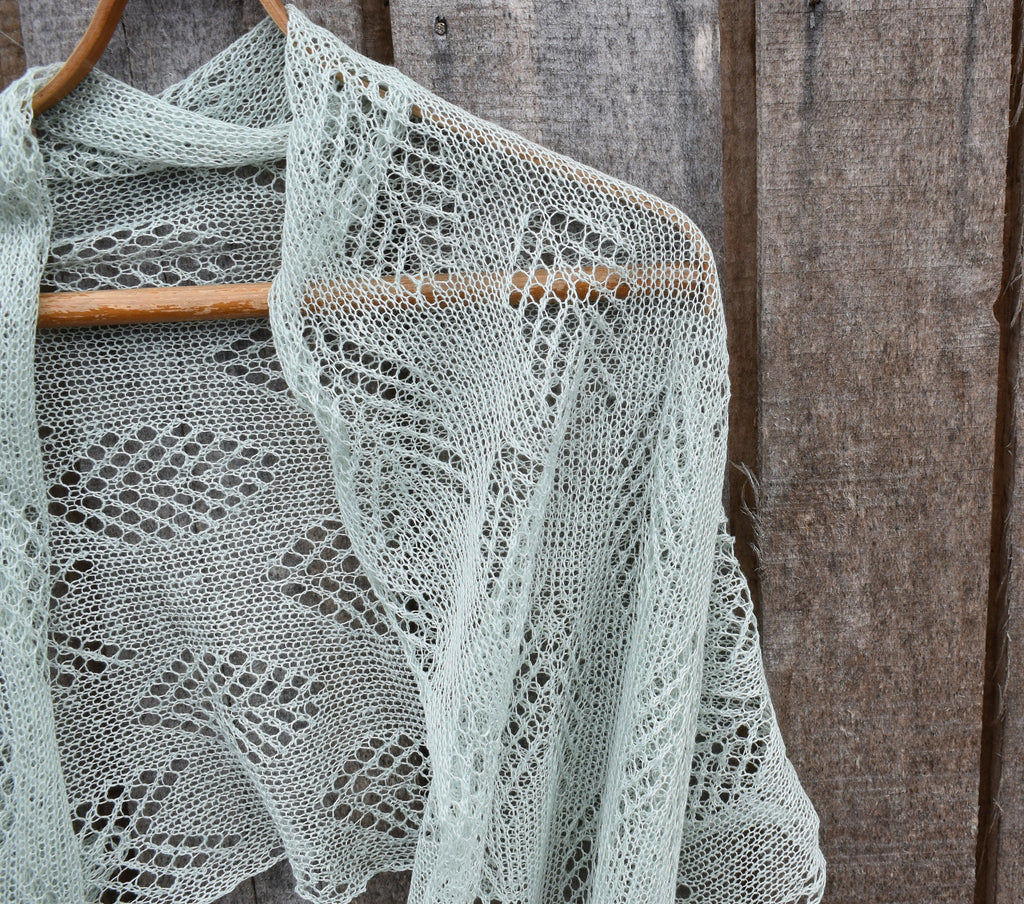 Knitted shawl with lace pattern on a wooden hanger against a rustic wooden background