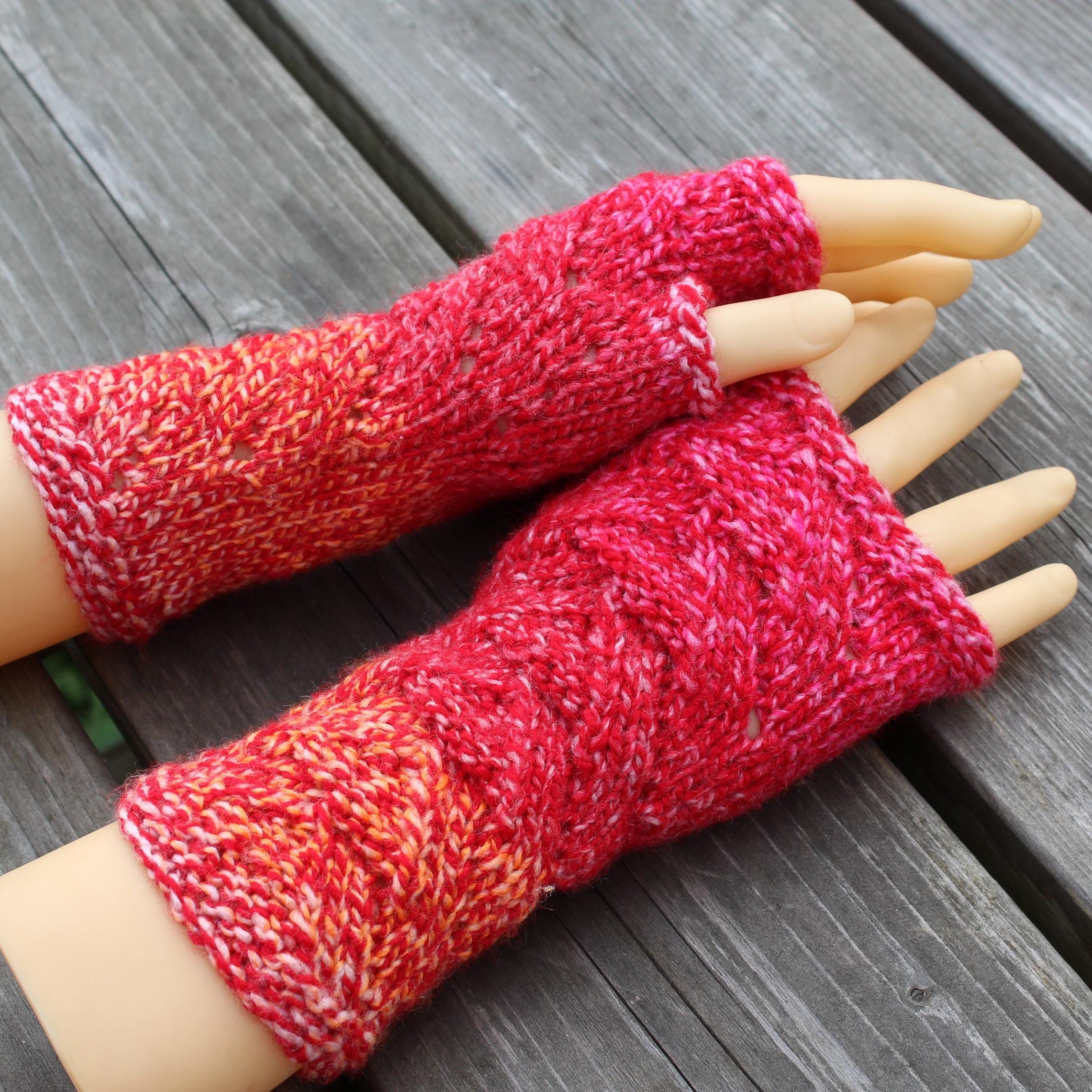 Red and pink knitted arm warmers on a mannequin arm against a wooden background