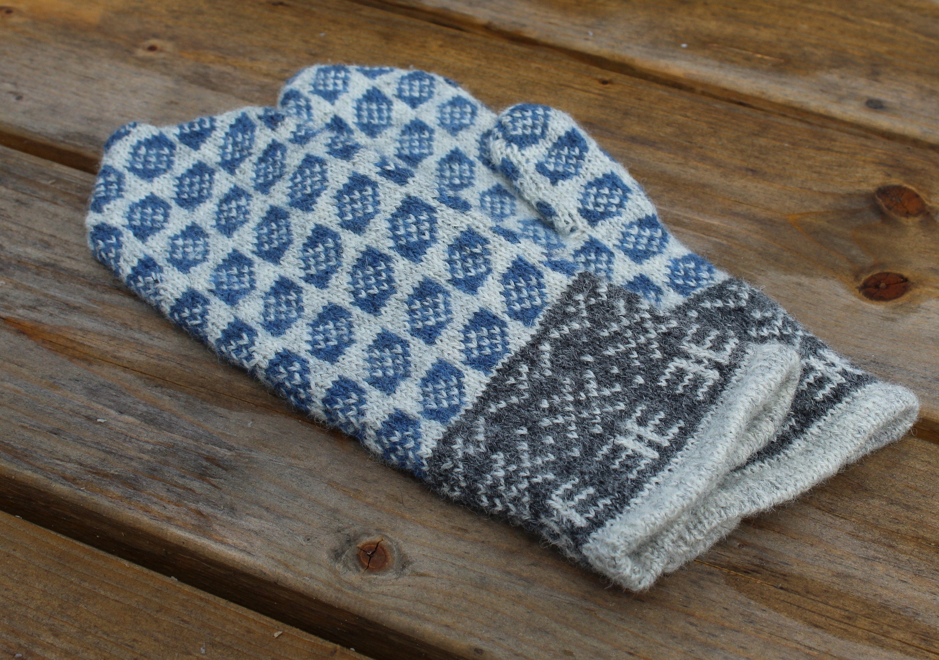 Pair of blue and gray patterned mittens on a wooden surface