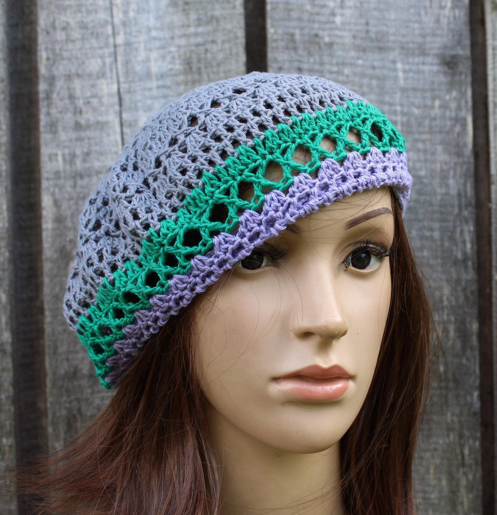 Crocheted hat with green and purple patterns on a mannequin head against a wooden background