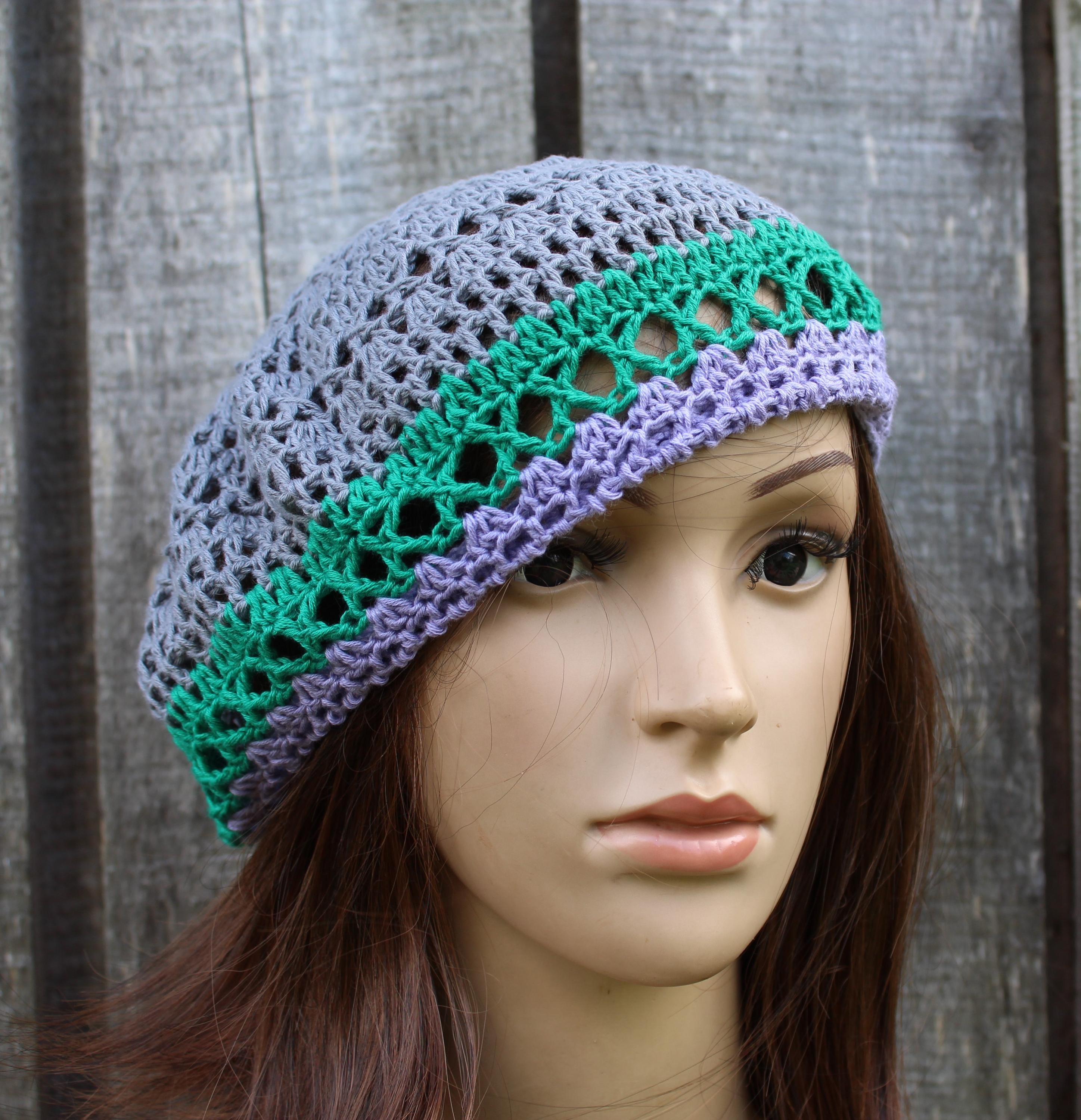 Crocheted hat with green and purple patterns on a mannequin head against a wooden background