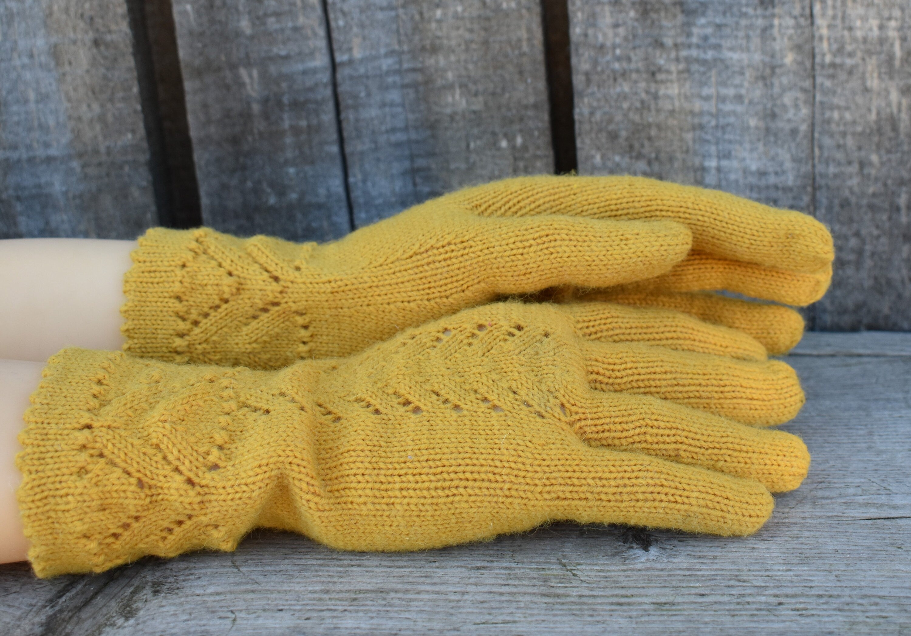 Yellow knitted gloves on a wooden surface with a wooden background