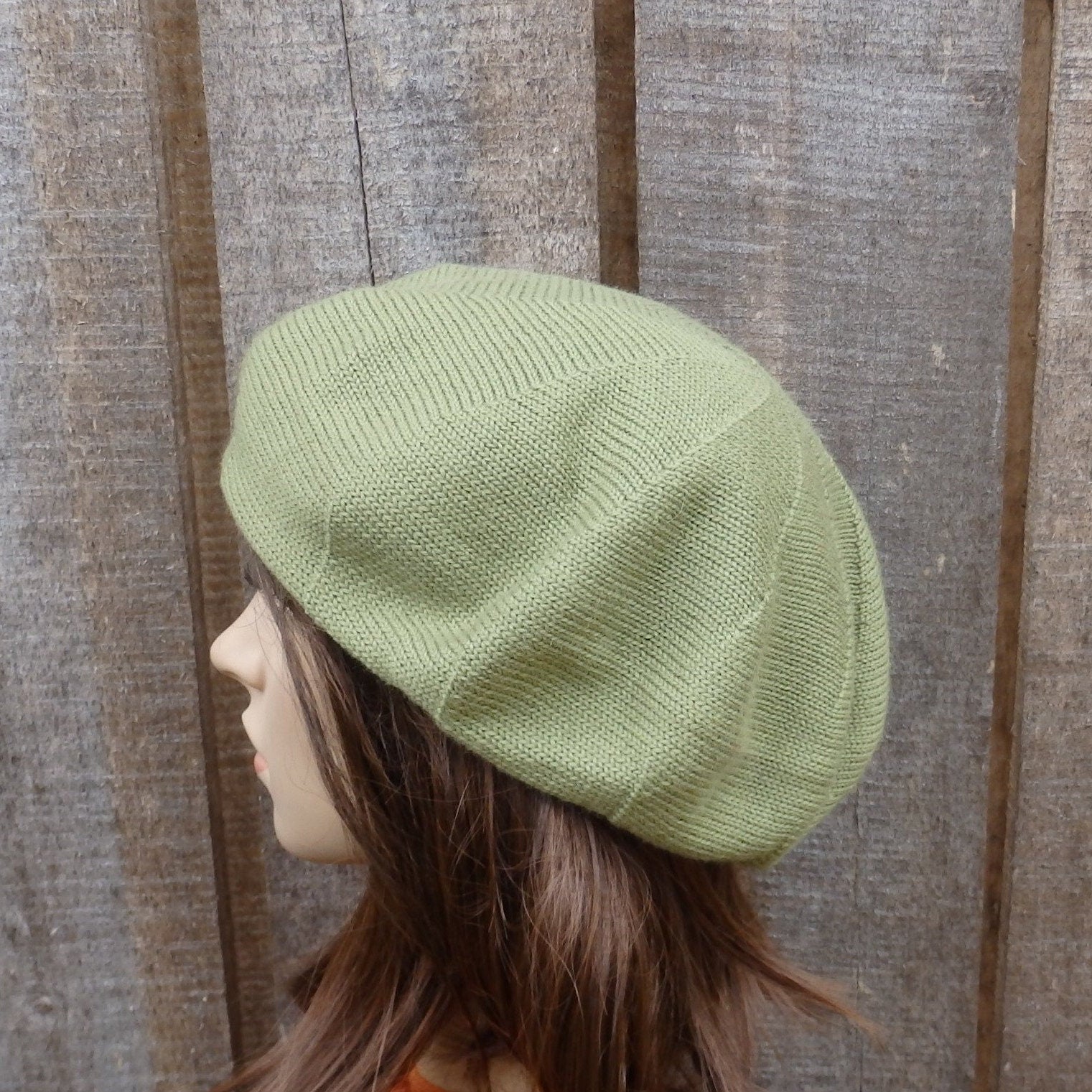 Green knit beret on a mannequin head against a wooden panel background