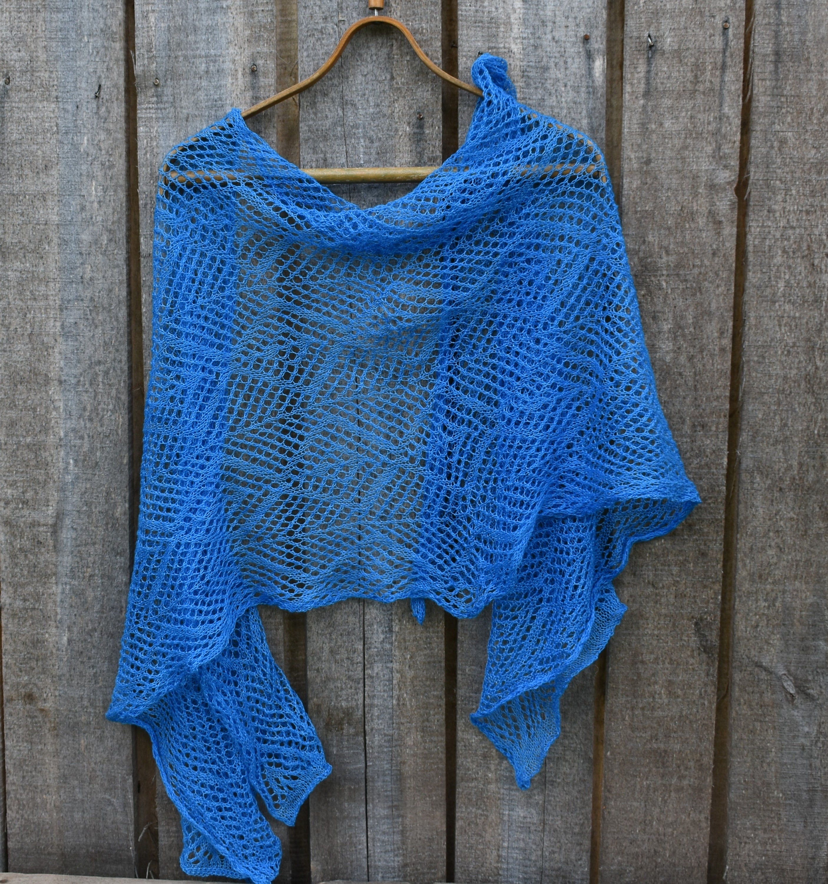Lightweight knitted shawl on a wooden hanger against a wooden background