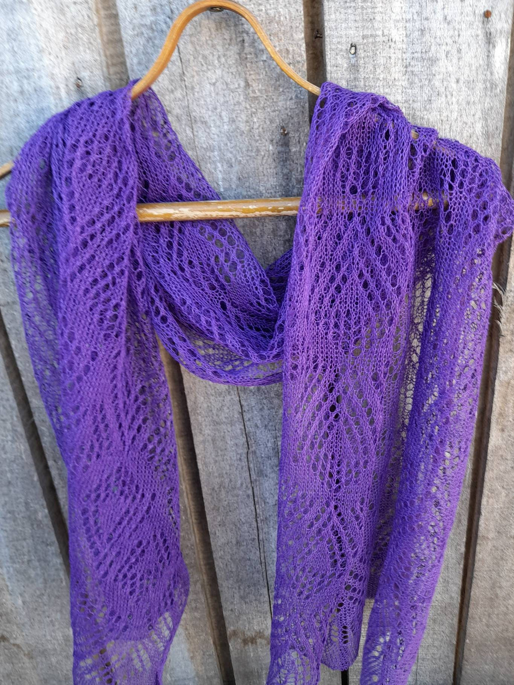 Purple knitted scarf on a wooden hanger against a wooden background