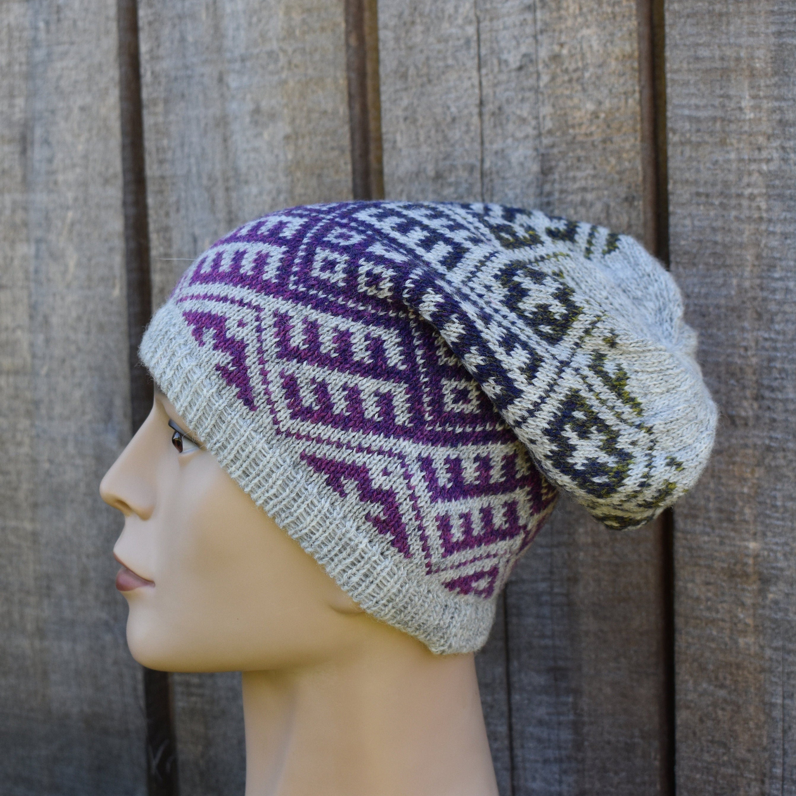Knitted hat with purple and gray pattern on a mannequin head against a wooden background