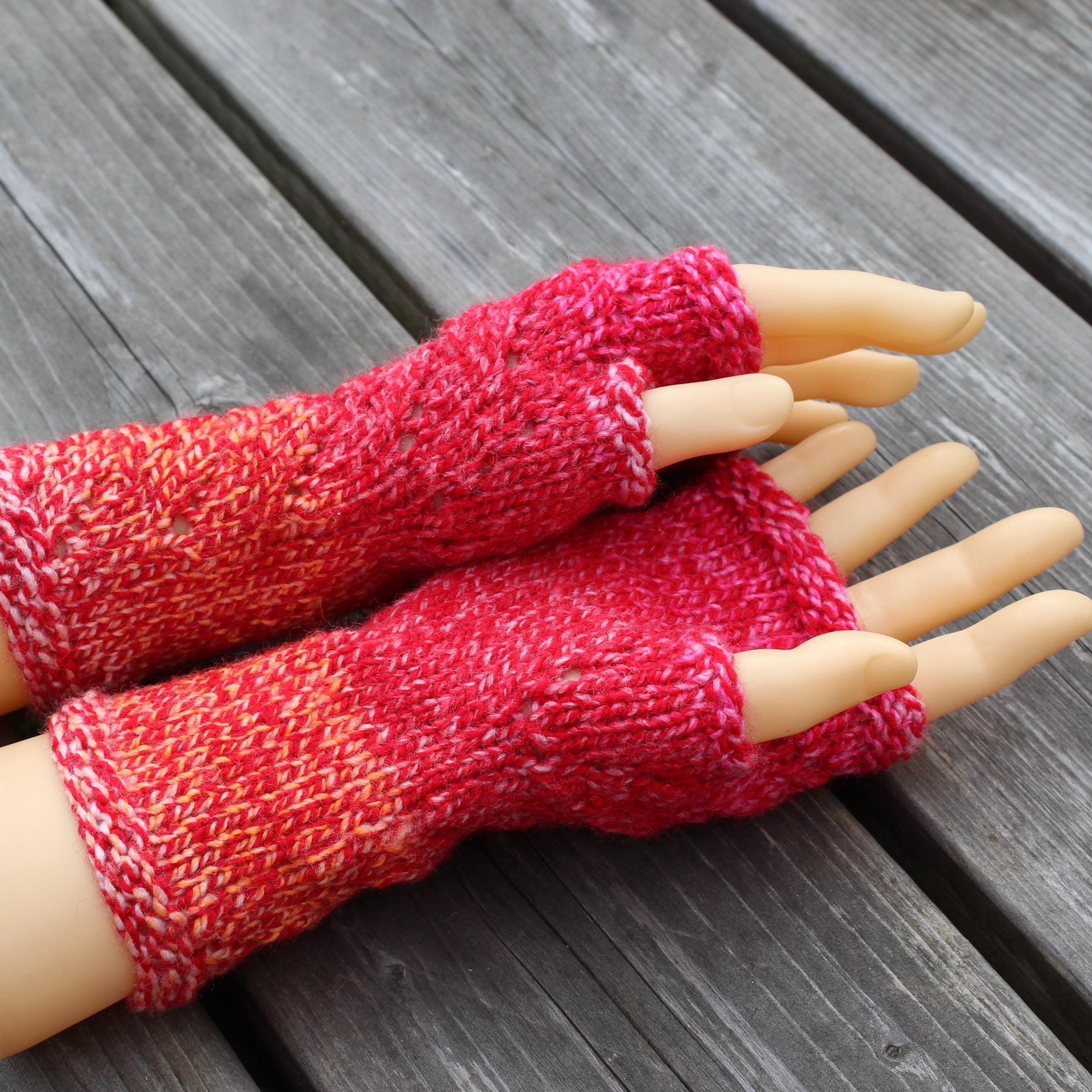 Red knitted fingerless gloves on a mannequin hand against a wooden background