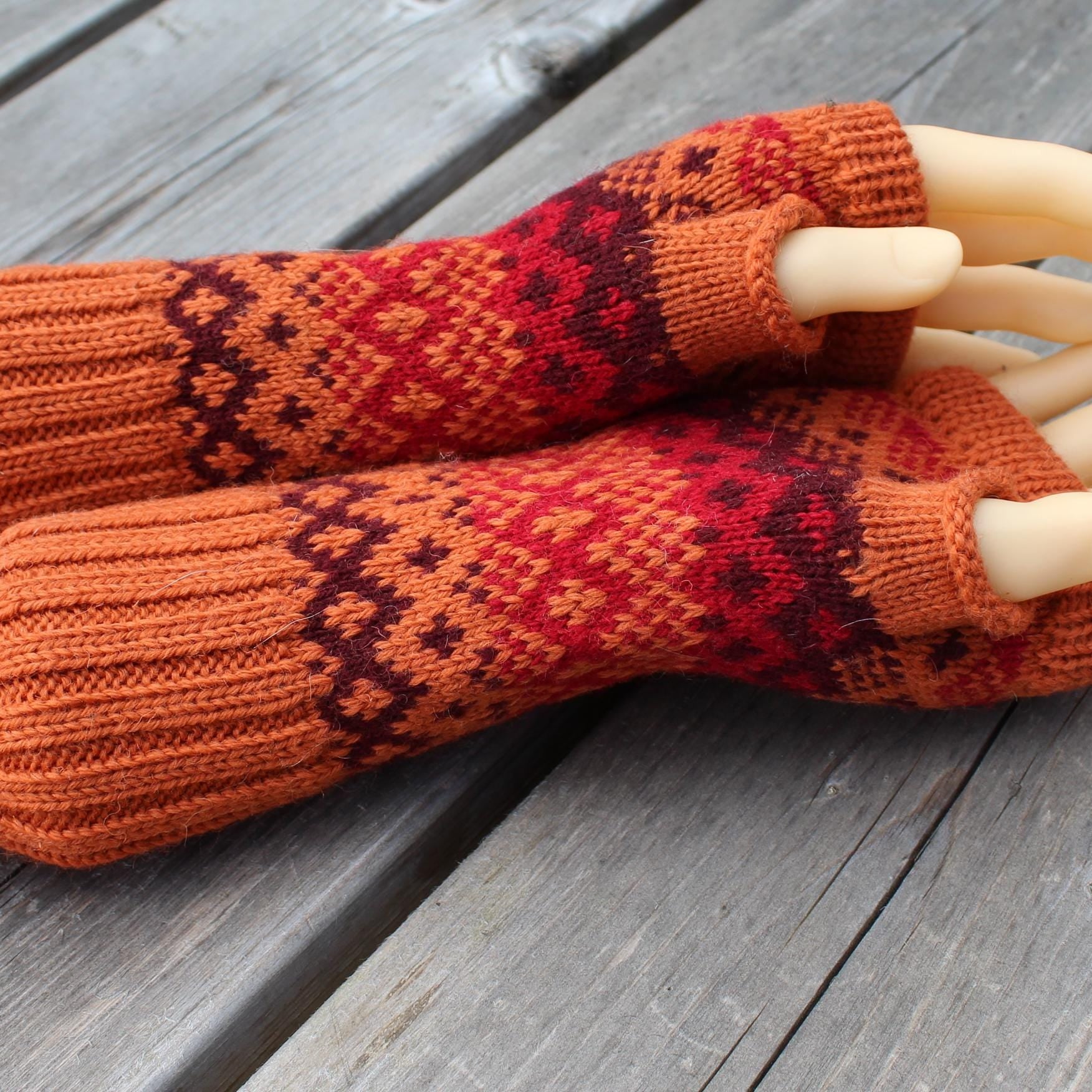 Pair of orange and red patterned fingerless gloves on a wooden surface