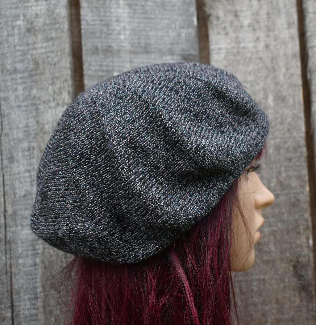 Person wearing a textured gray knit beret against a wooden fence background