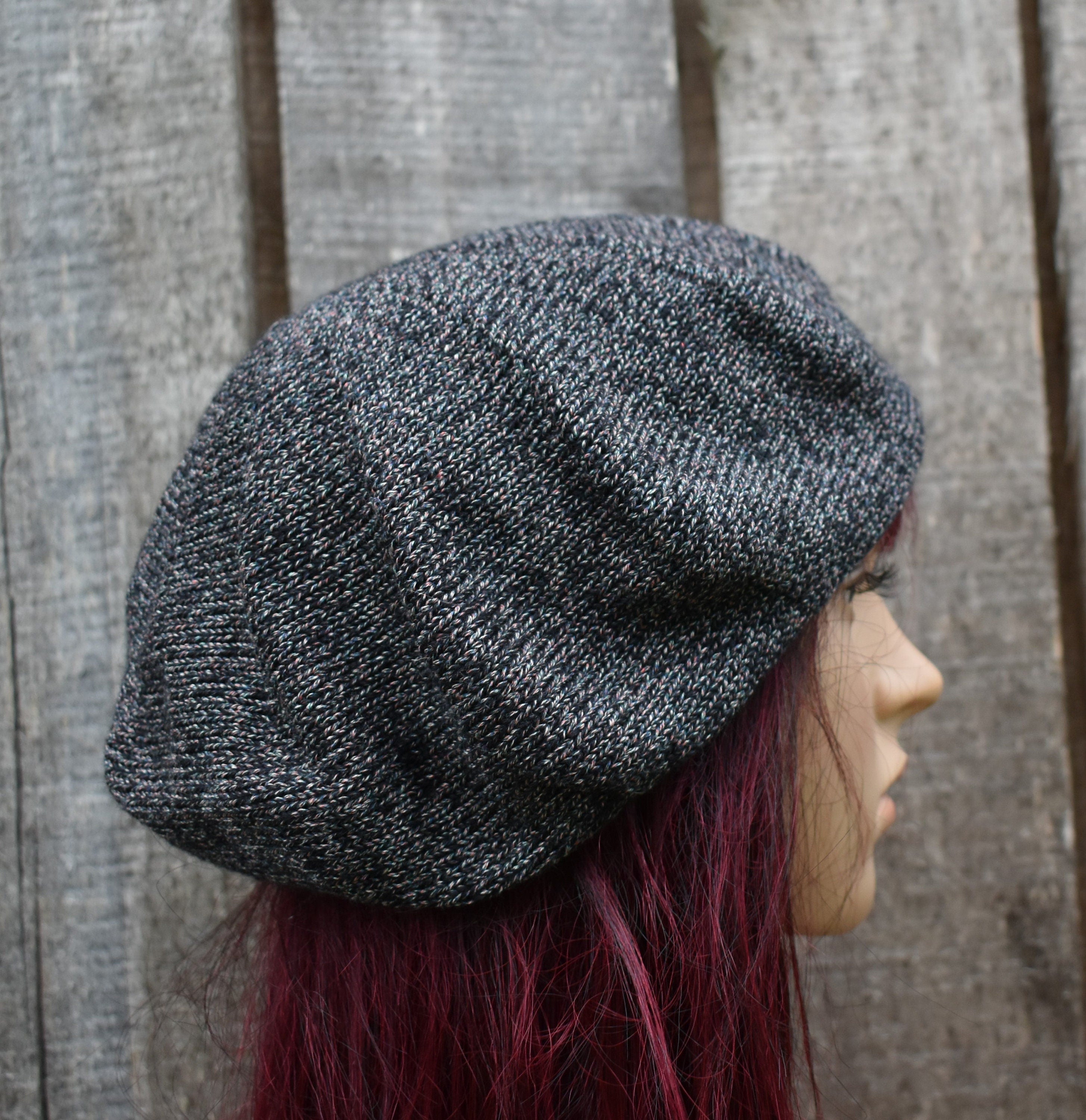 Person wearing a textured gray knit beret against a wooden fence background