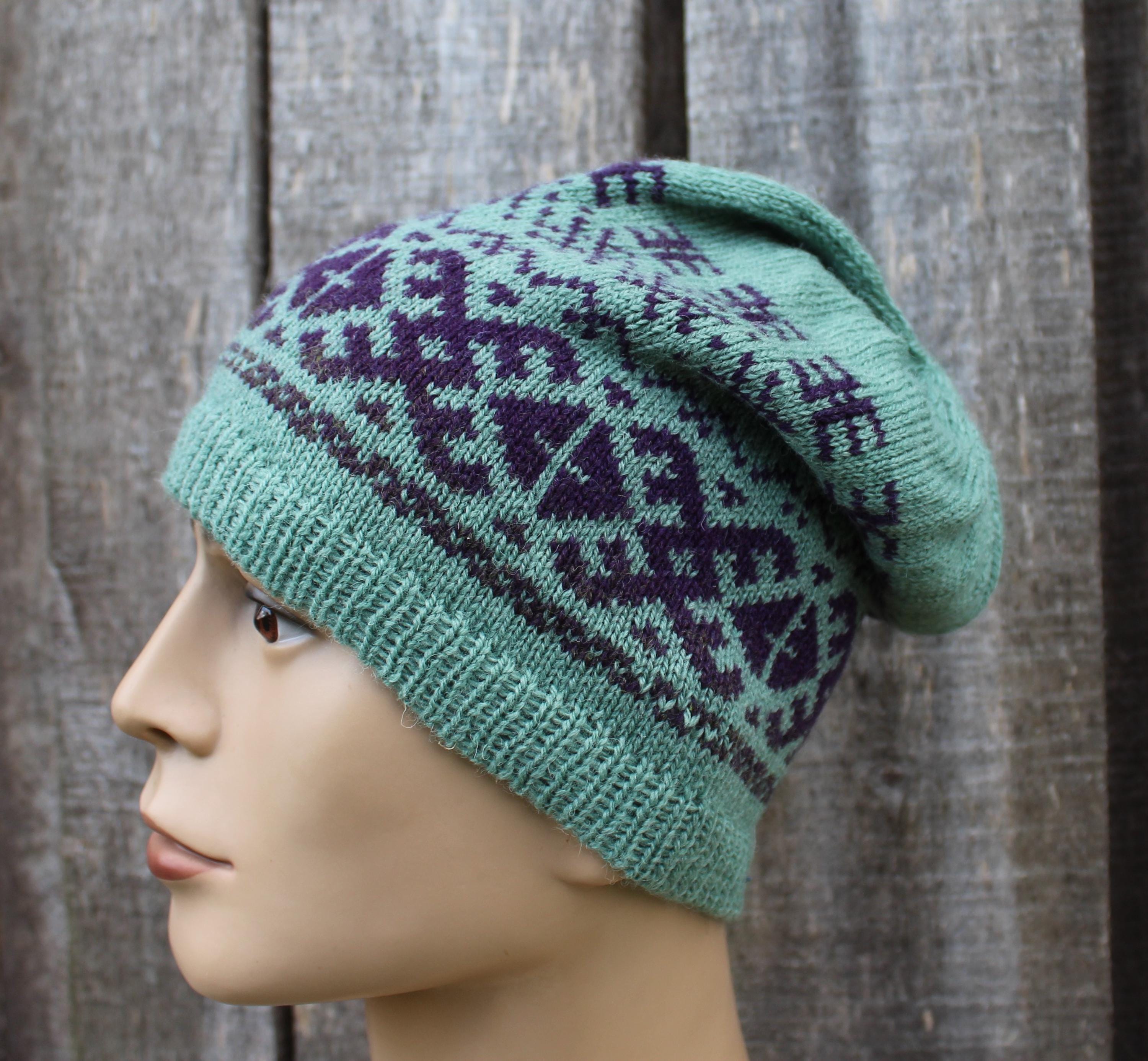 Green knitted hat with purple patterns on a mannequin head against a wooden background