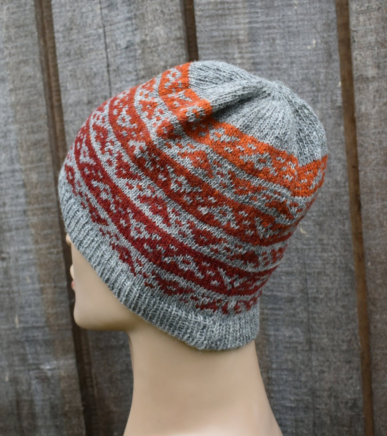 Knitted hat with gray and orange pattern on a mannequin head against a wooden background