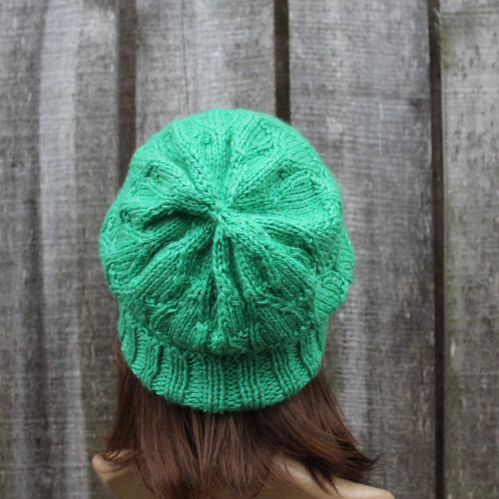 Green knitted beanie worn by a person against a wooden background