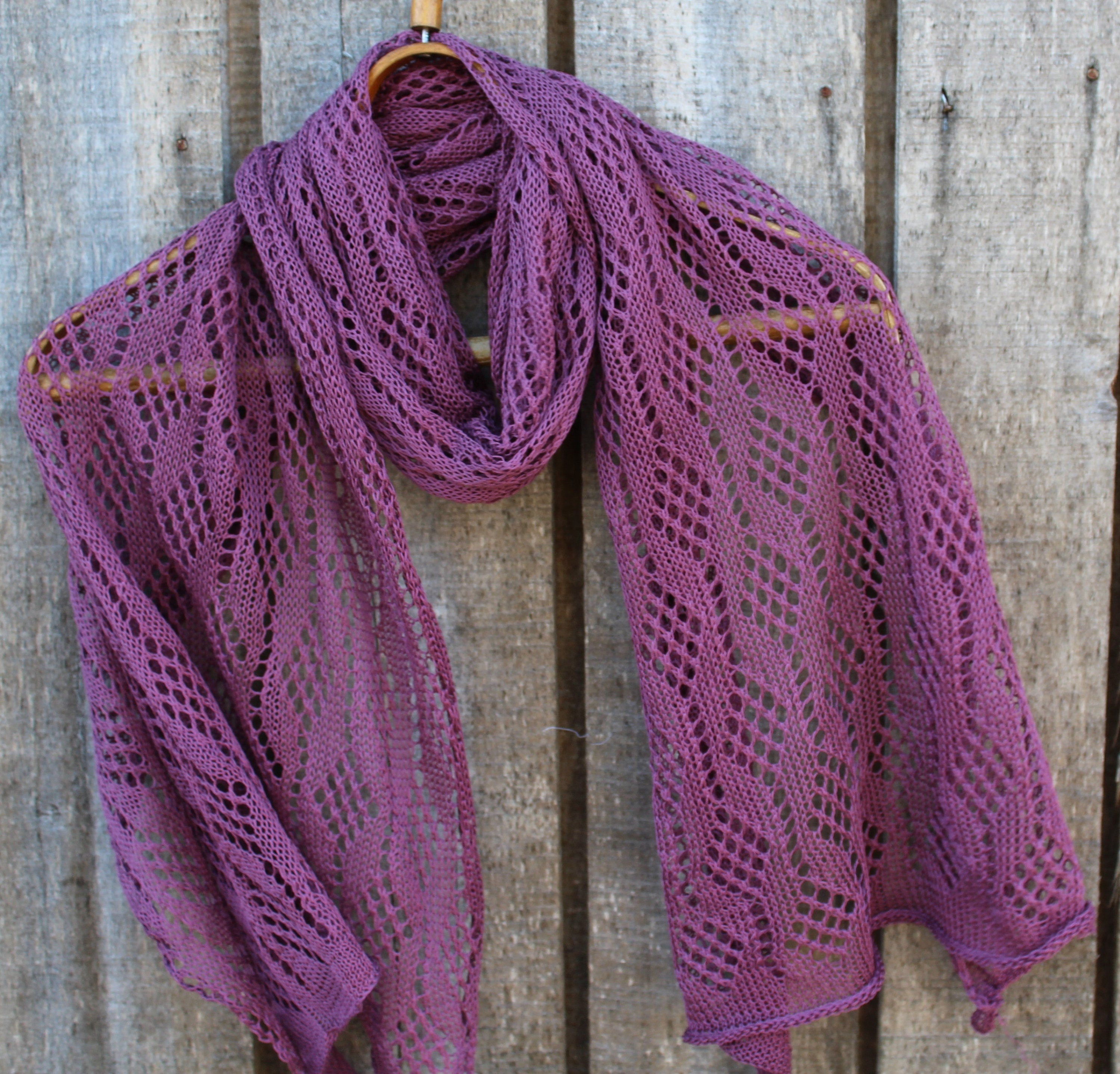 Purple knitted shawl on a wooden hanger against a wooden background