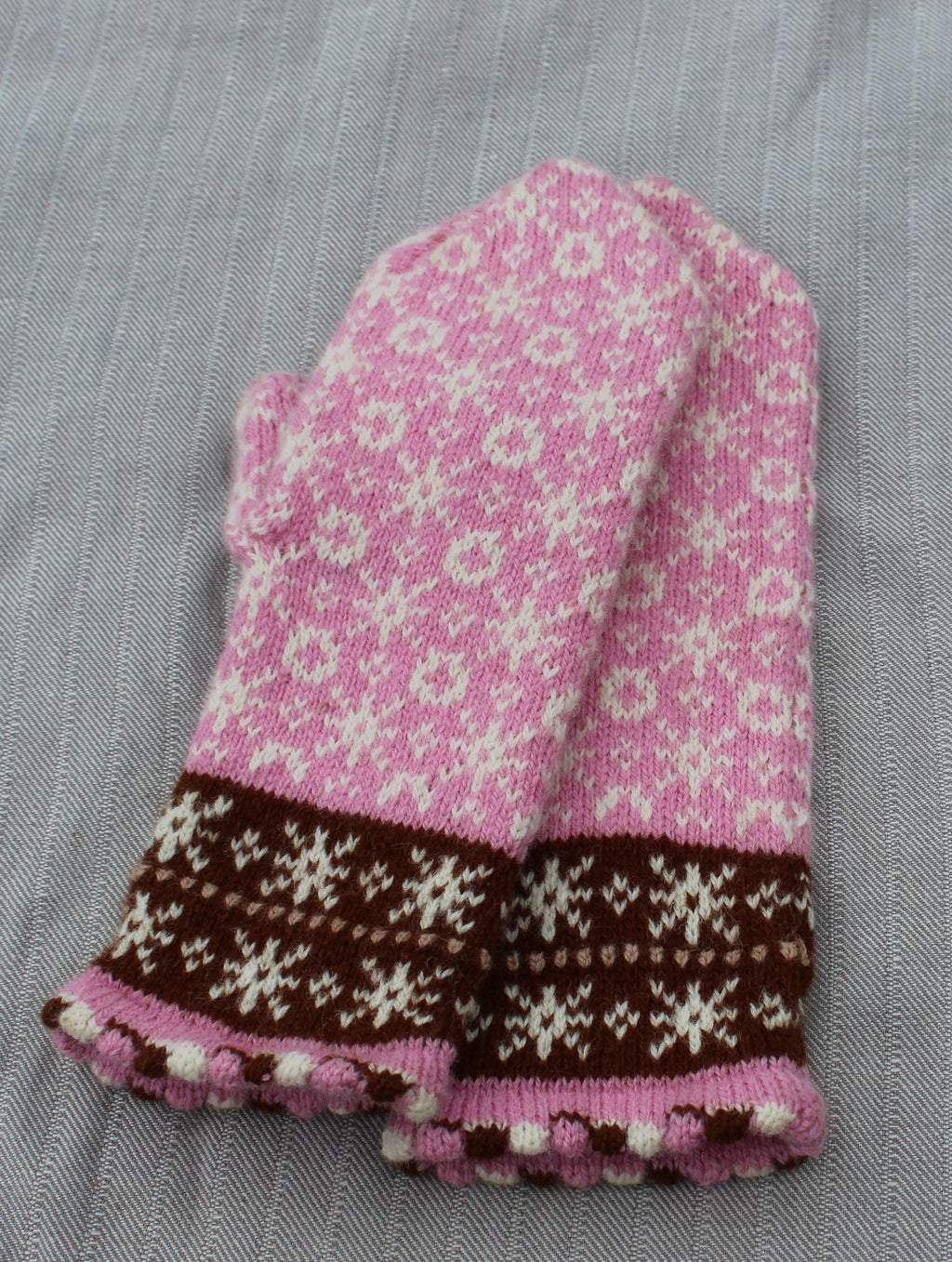Knitted pink and brown mitten with a floral pattern on a gray fabric background