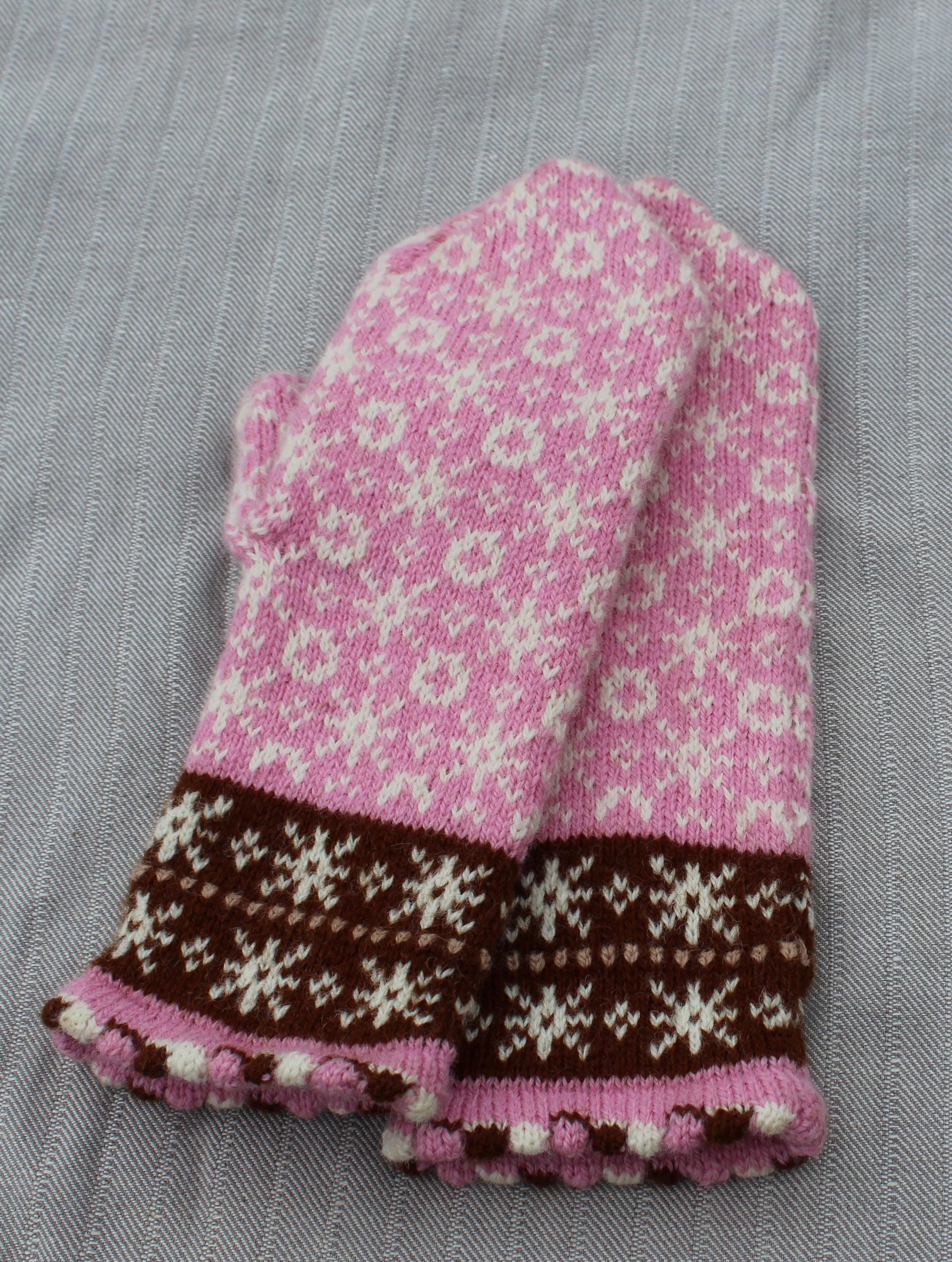 Knitted pink and brown mitten with a floral pattern on a gray fabric background