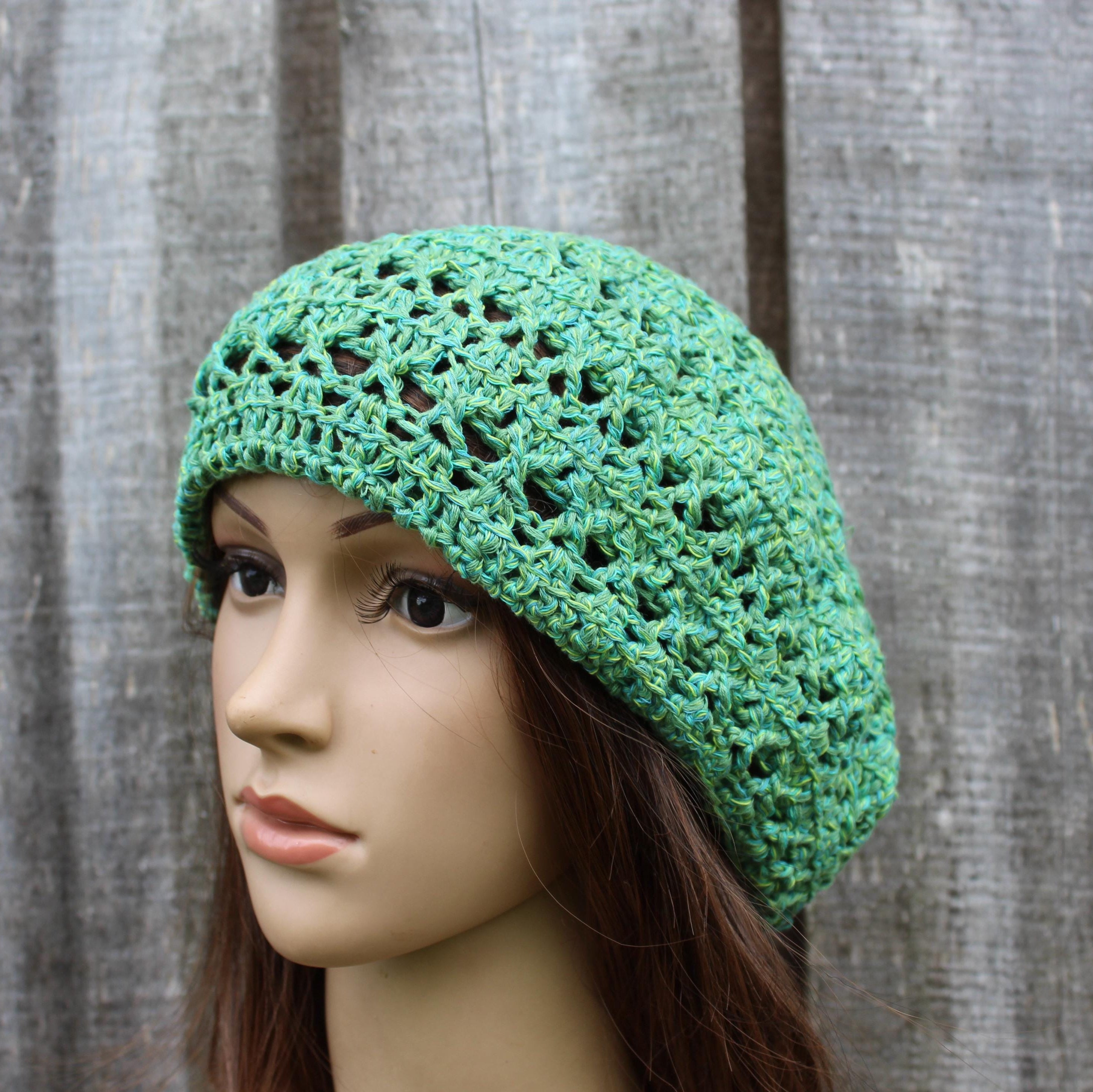 Green crochet hat on a mannequin head against a wooden background