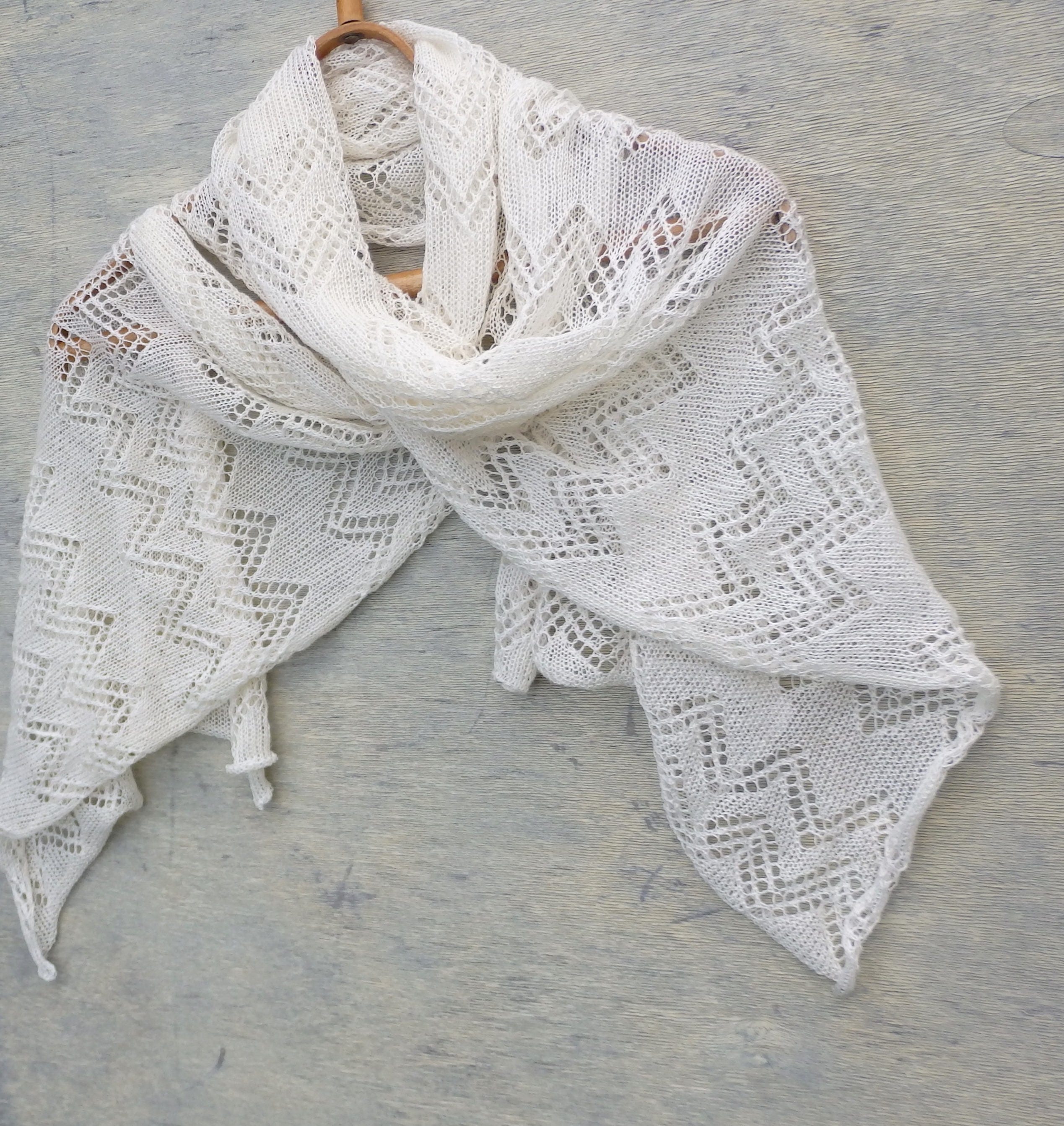 White lace shawl on a wooden hanger against a gray wooden background