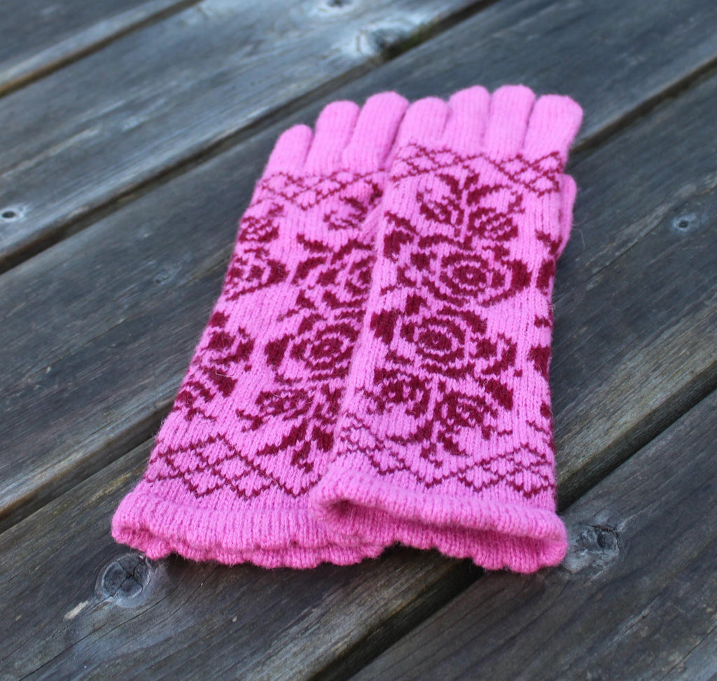 Pair of pink knitted gloves with a pattern on a wooden surface